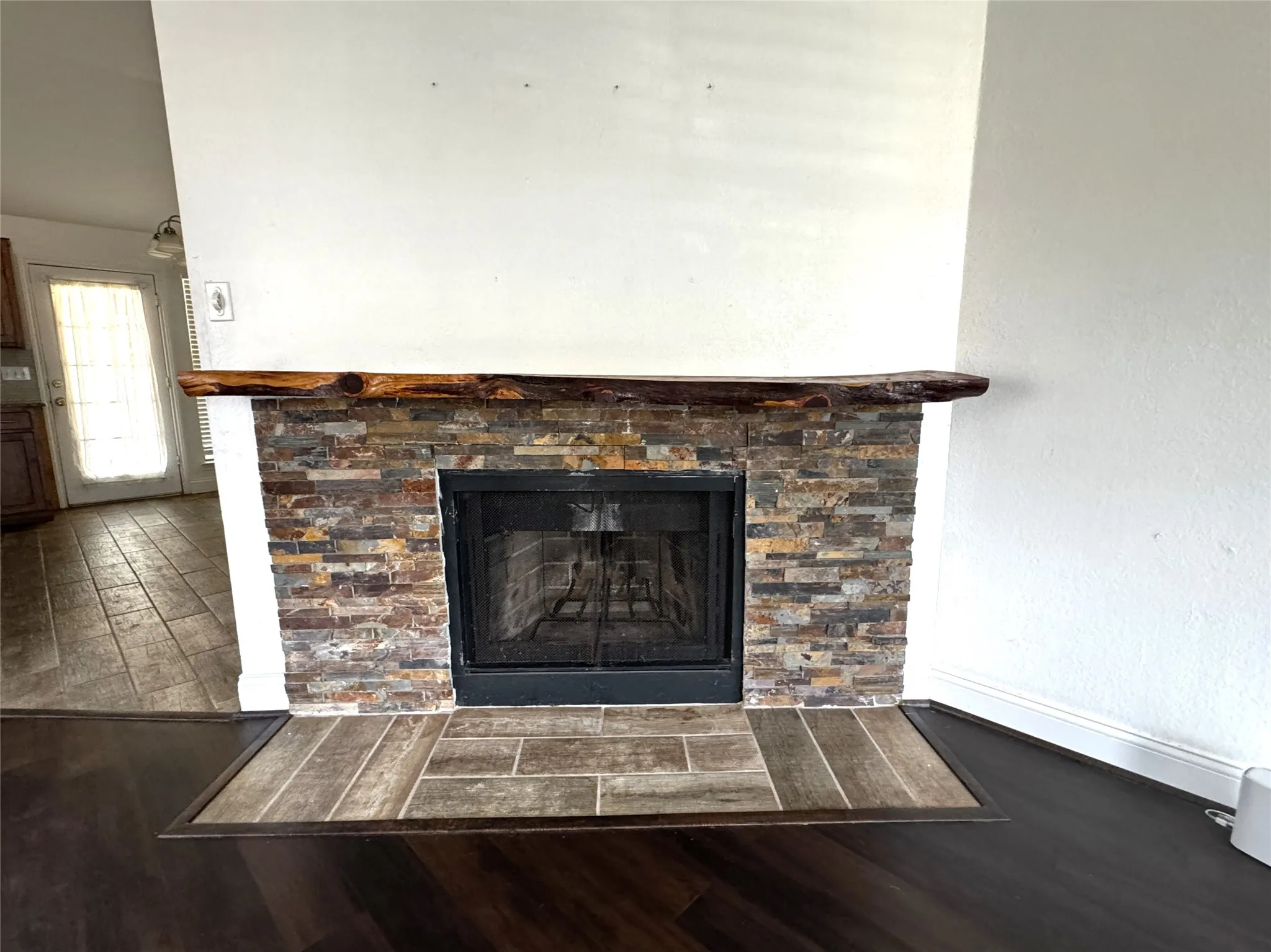 Fireplace featuring a stone tile surround, a natural wood mantle, and a black firebox with a screen