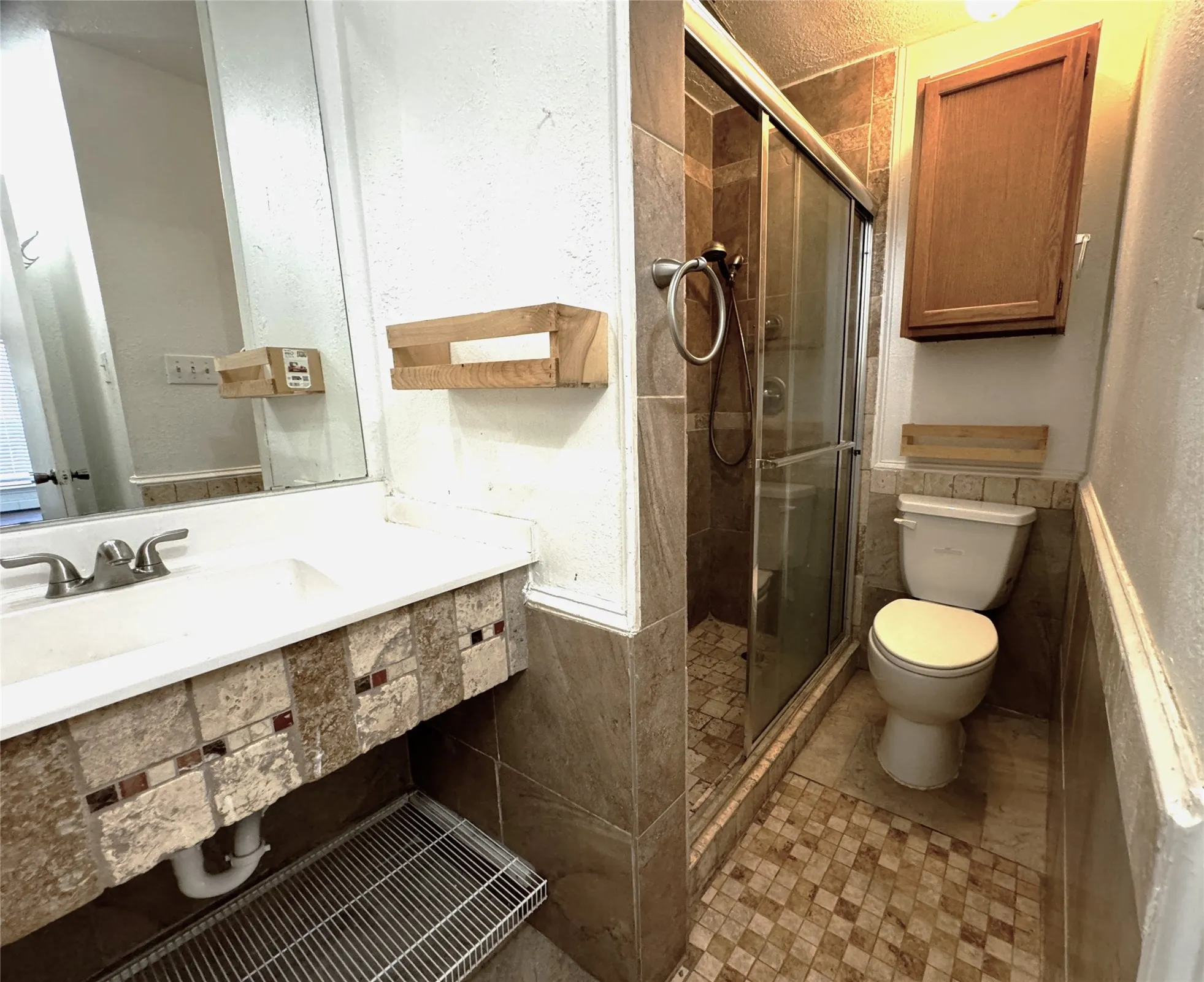 Full bathroom featuring a walk-in shower with glass enclosure, mosaic tile flooring, tiled vanity with integrated sink, and an overhead storage cabinet