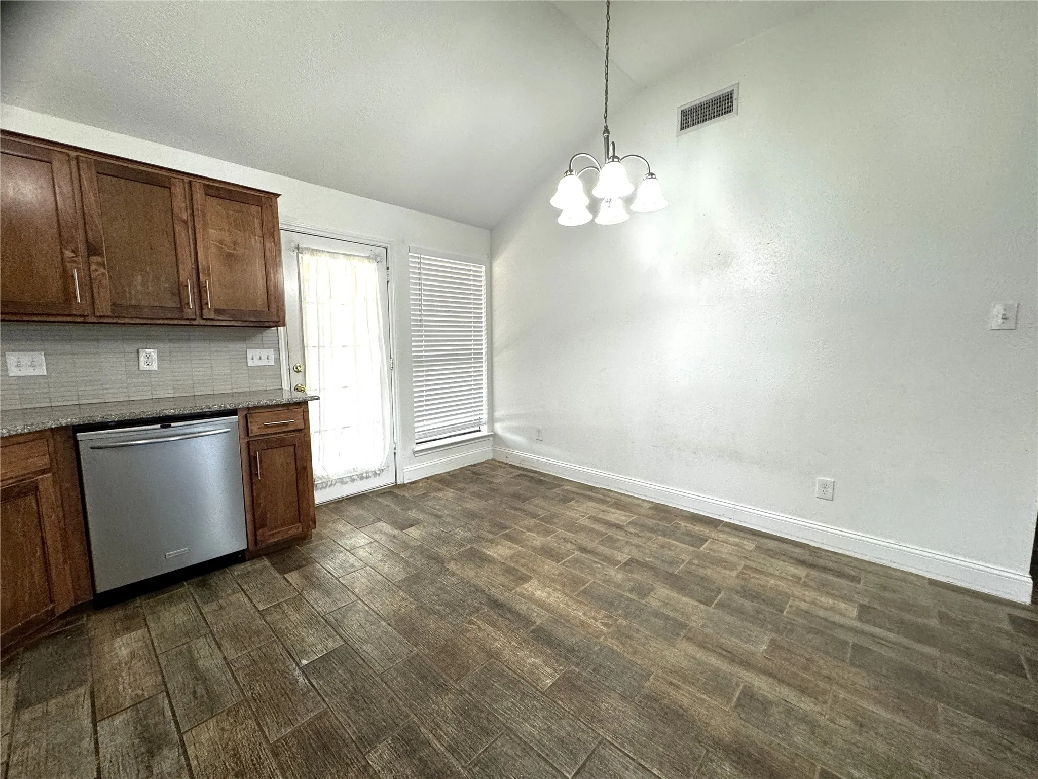 Wood-finish plank flooring, stainless steel dishwasher, wood cabinetry, stone-finish countertop, and tile backsplash