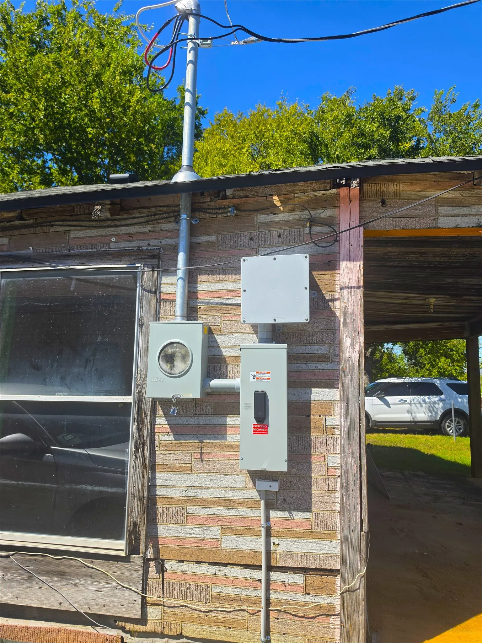 Electrical service entrance with conduit and meter box, mounted on exterior wall with textured paneling and window