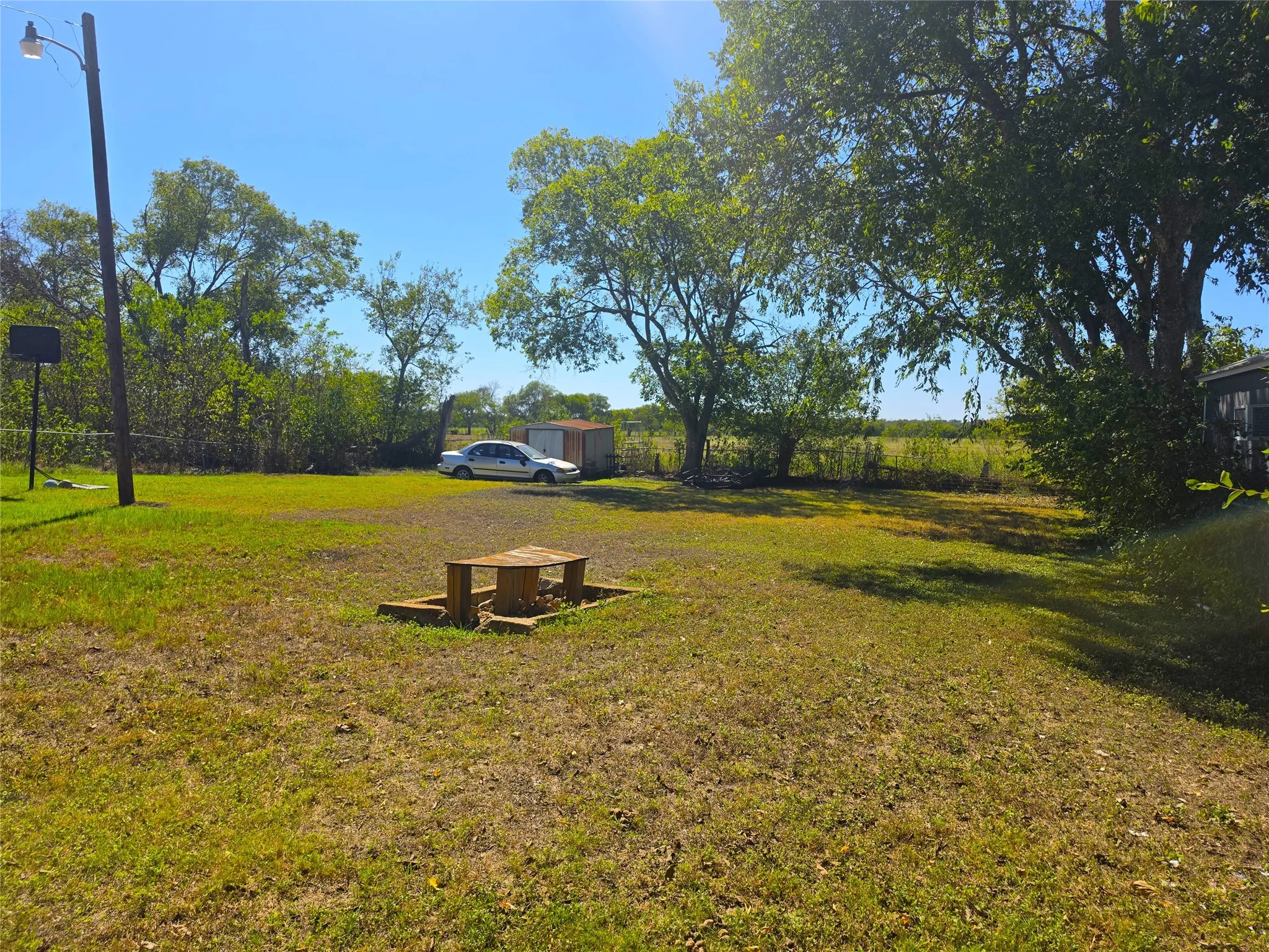Expansive grassy area with mature trees, featuring a wooden picnic table and a storage shed