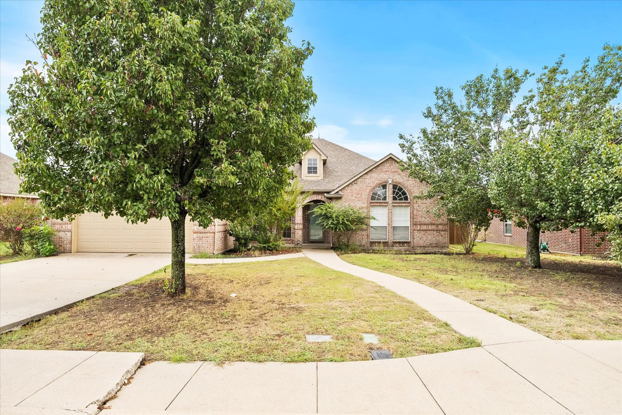 Brick exterior residence with a two-car garage, dormer window, and arched window accent