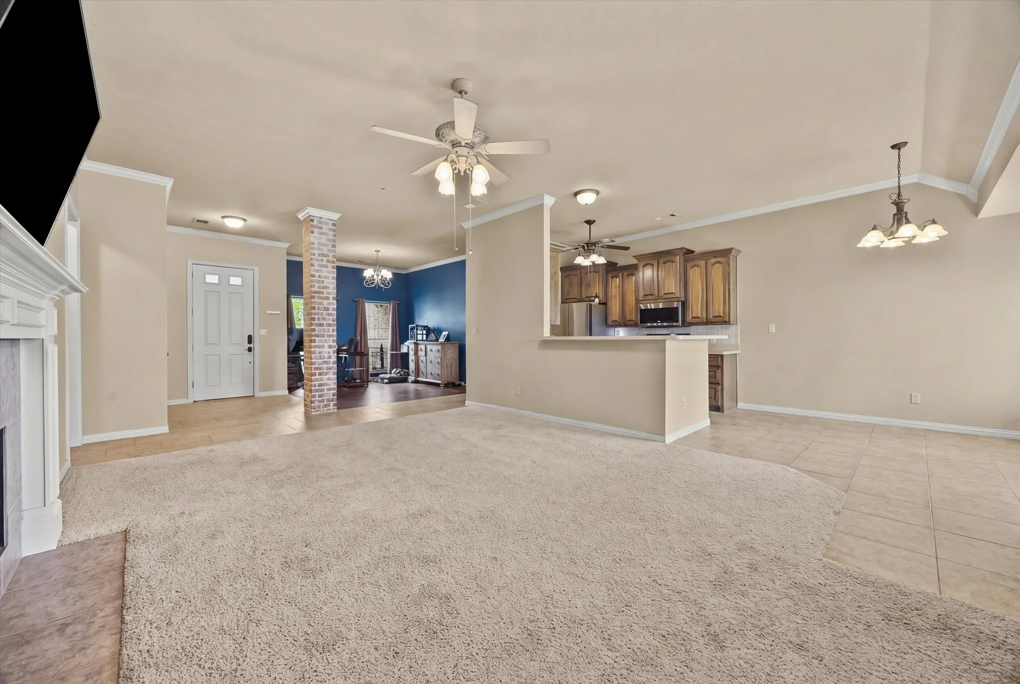 Open-concept living area featuring a fireplace with a mantel, ceiling fan, and mixed flooring with carpeting and tile