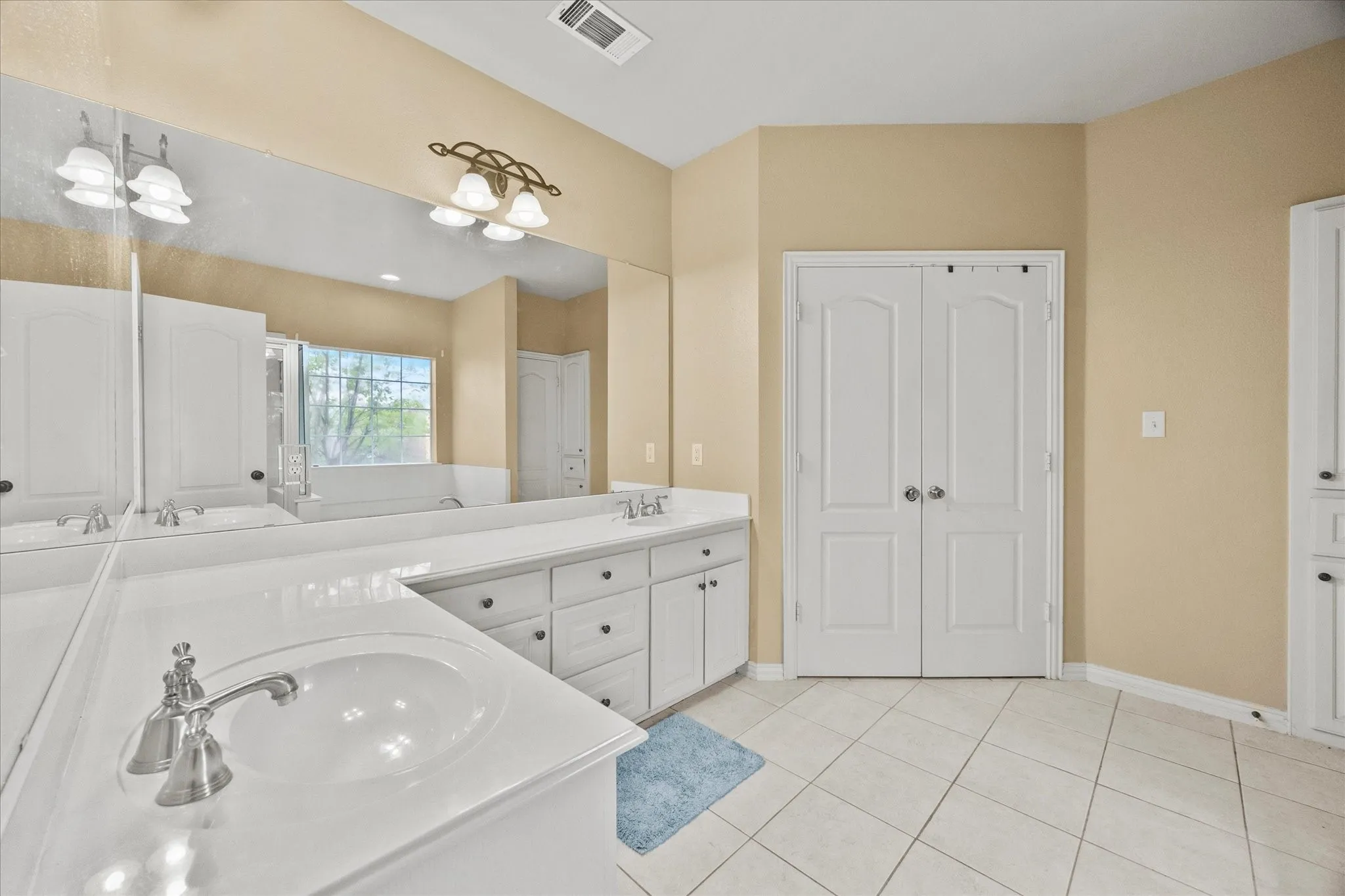 Dual vanity with integrated sinks and brushed nickel faucets, extensive mirror, white shaker-style cabinetry, and tile flooring