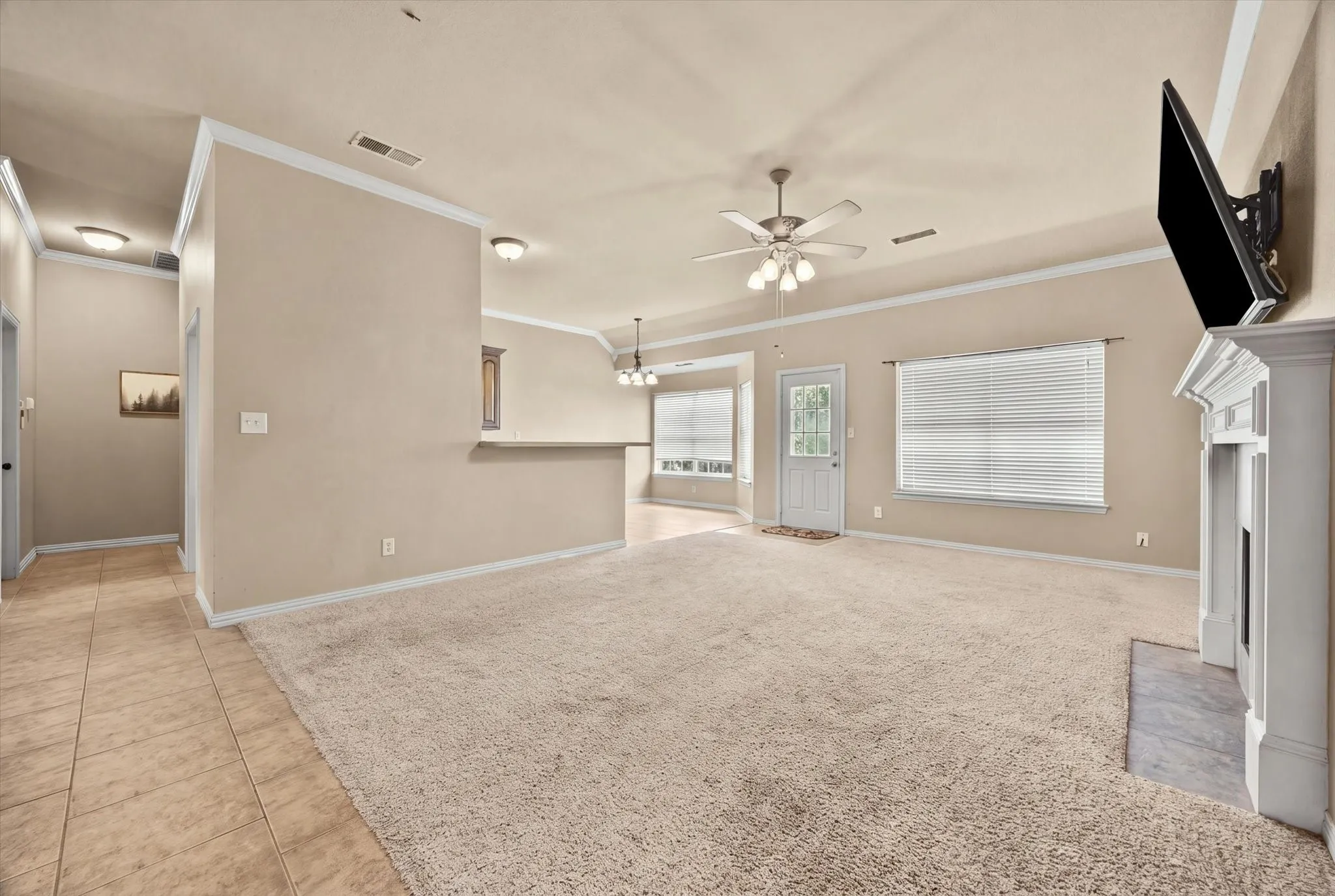 Spacious living area featuring a fireplace with a decorative mantel, carpeted flooring, and a ceiling fan