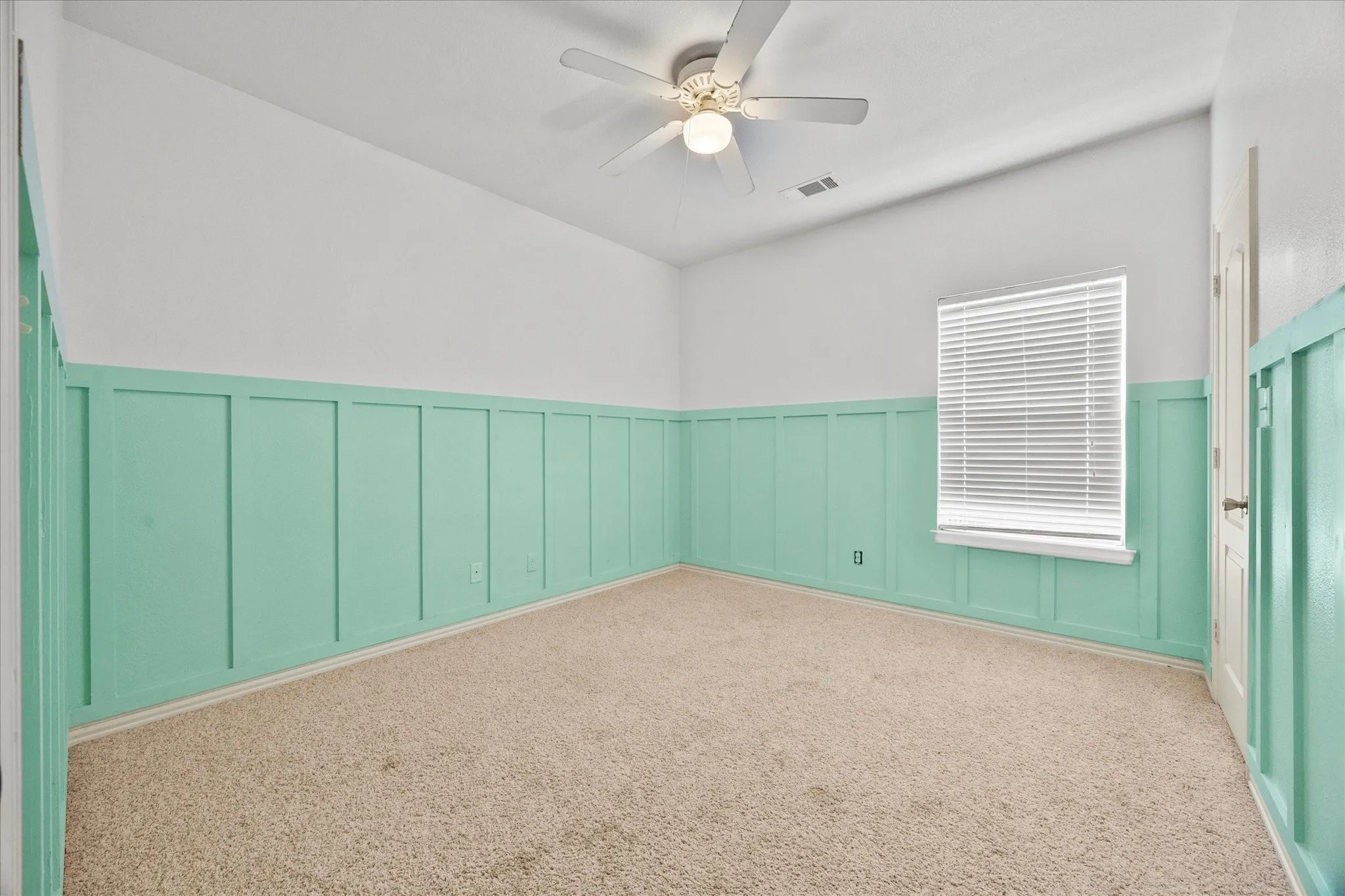 Angled ceiling, overhead ceiling fan with lighting, wall paneling, light-toned carpeting, and a window with blinds