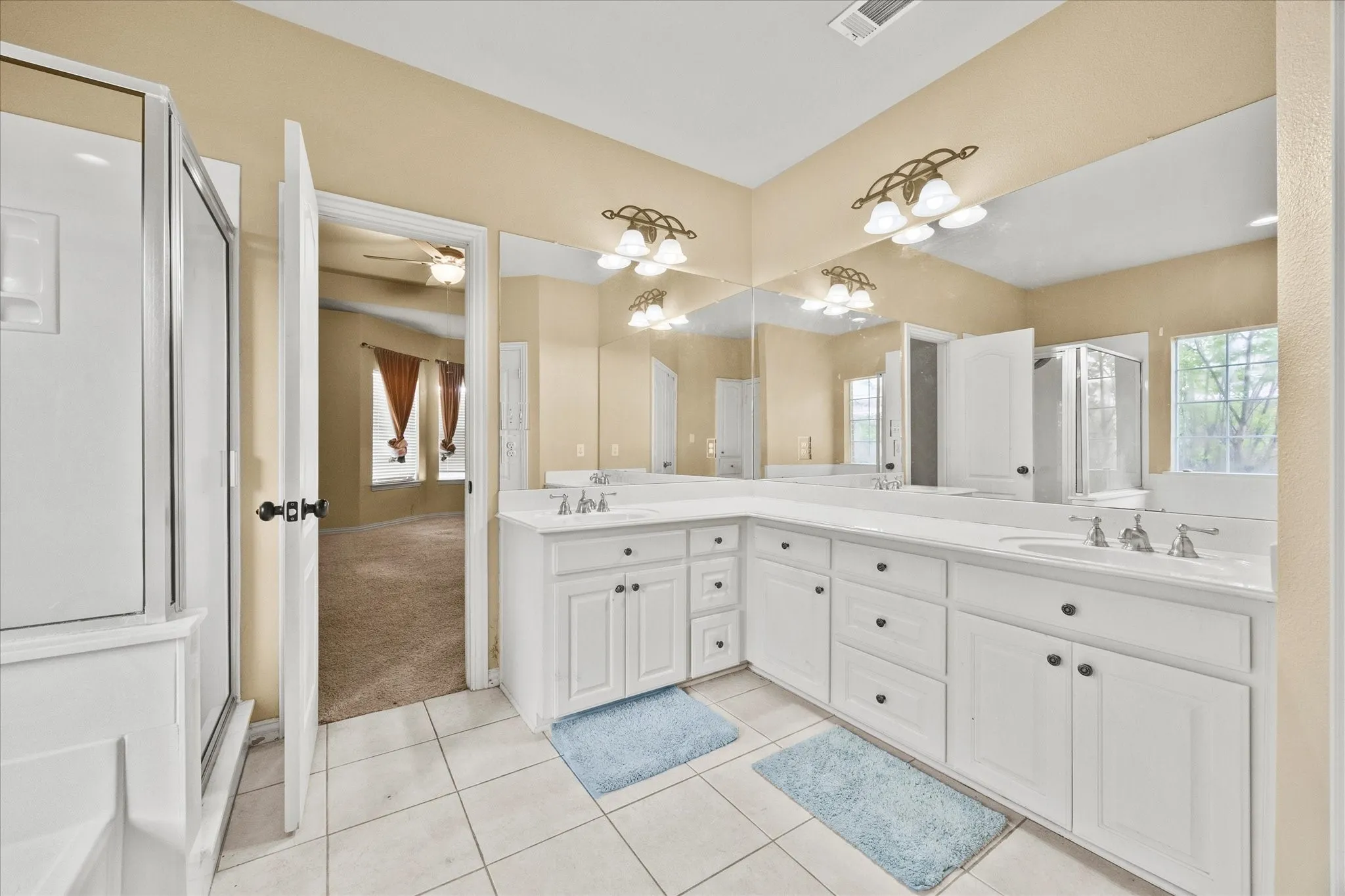 Spacious bathroom featuring a dual vanity with white cabinetry, extensive counter space, large mirrors, a glass-enclosed shower, and tile flooring