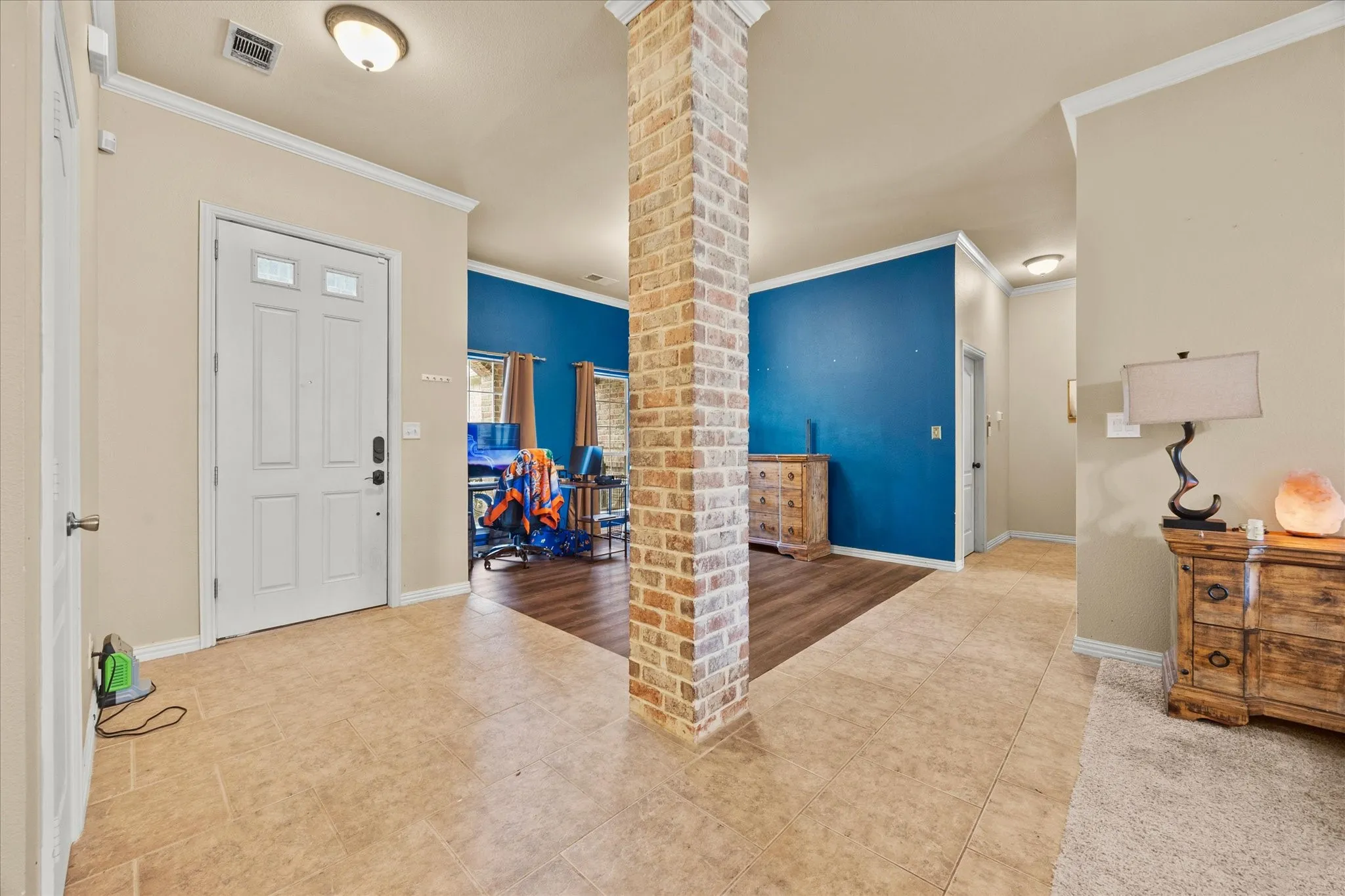 Entrance foyer featuring tile flooring, a brick column accent, and crown molding