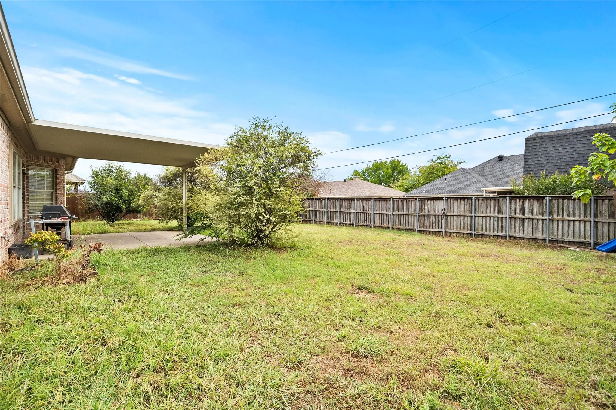Expansive backyard featuring a covered patio, mature tree, and wood privacy fencing
