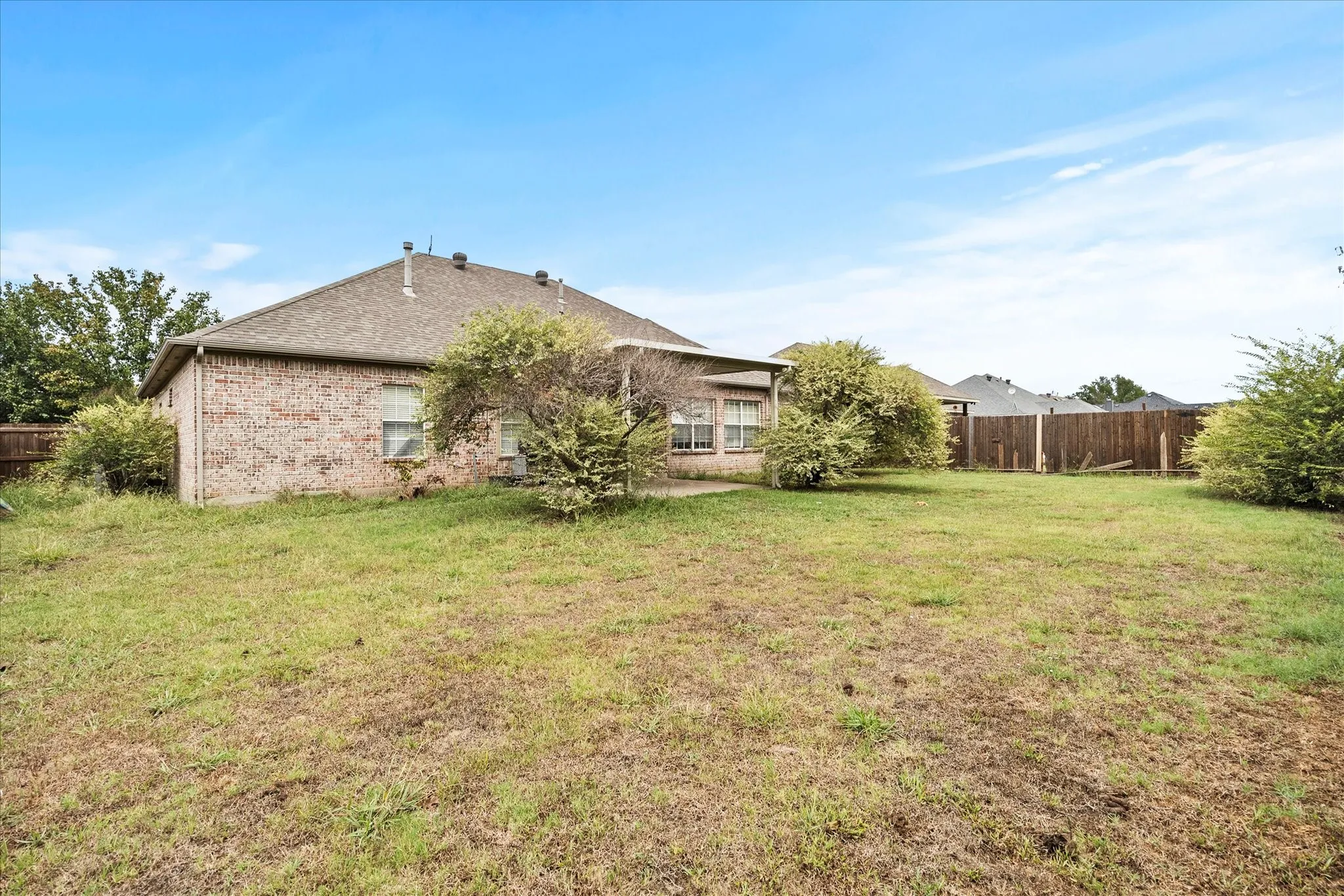 Expansive backyard featuring a partial wood fence, brick exterior, and a covered patio
