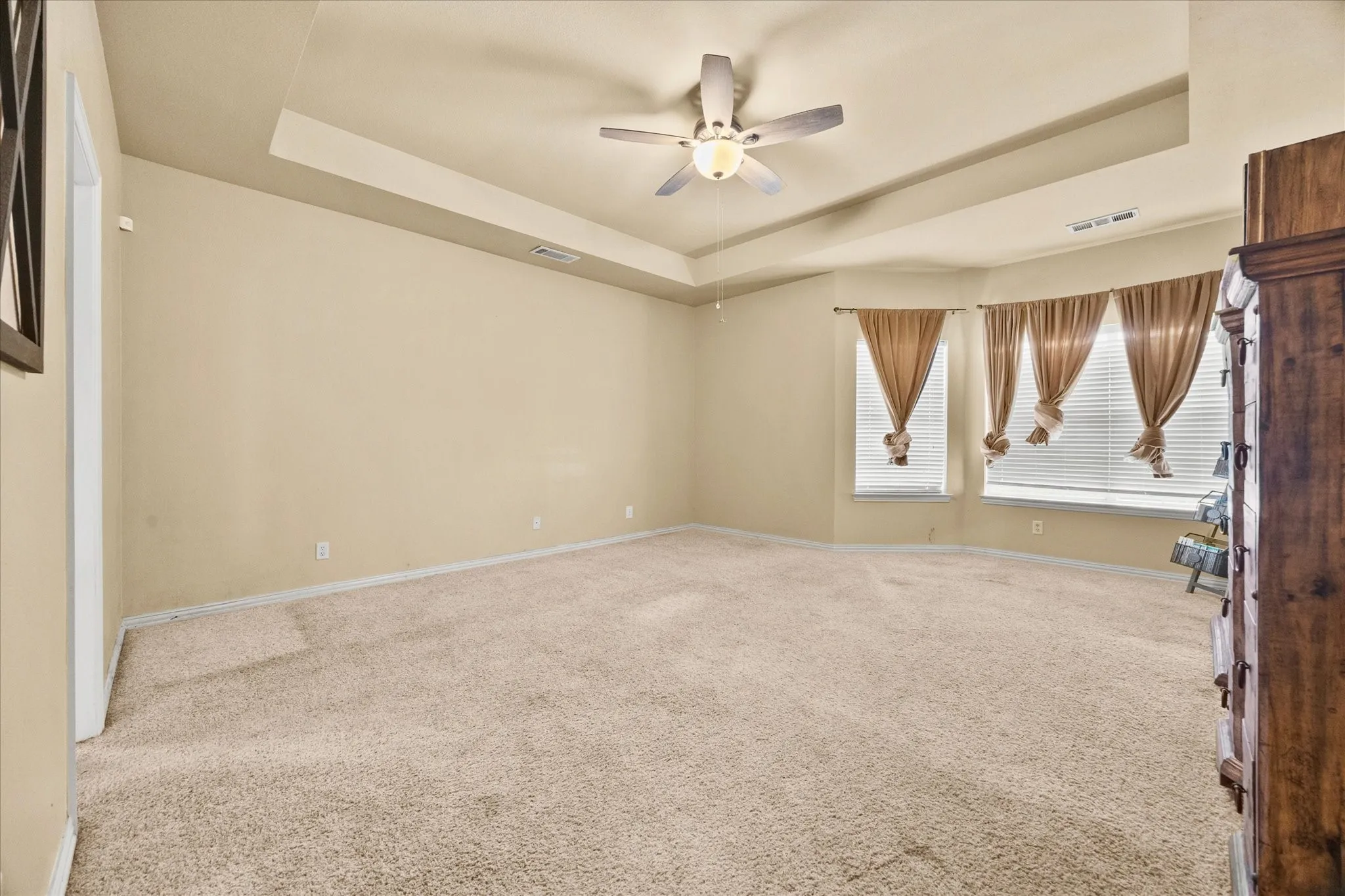 Spacious room featuring tray ceiling, ceiling fan, and carpeted flooring