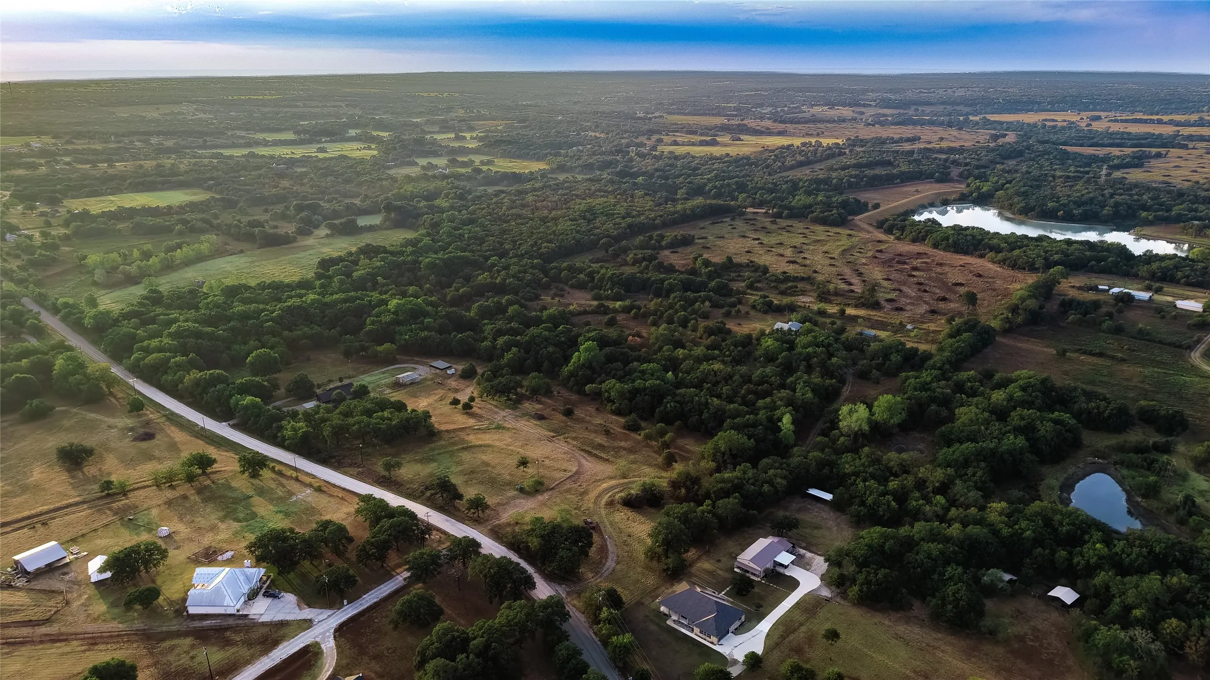 Expansive rural landscape featuring wooded areas, open fields, and bodies of water