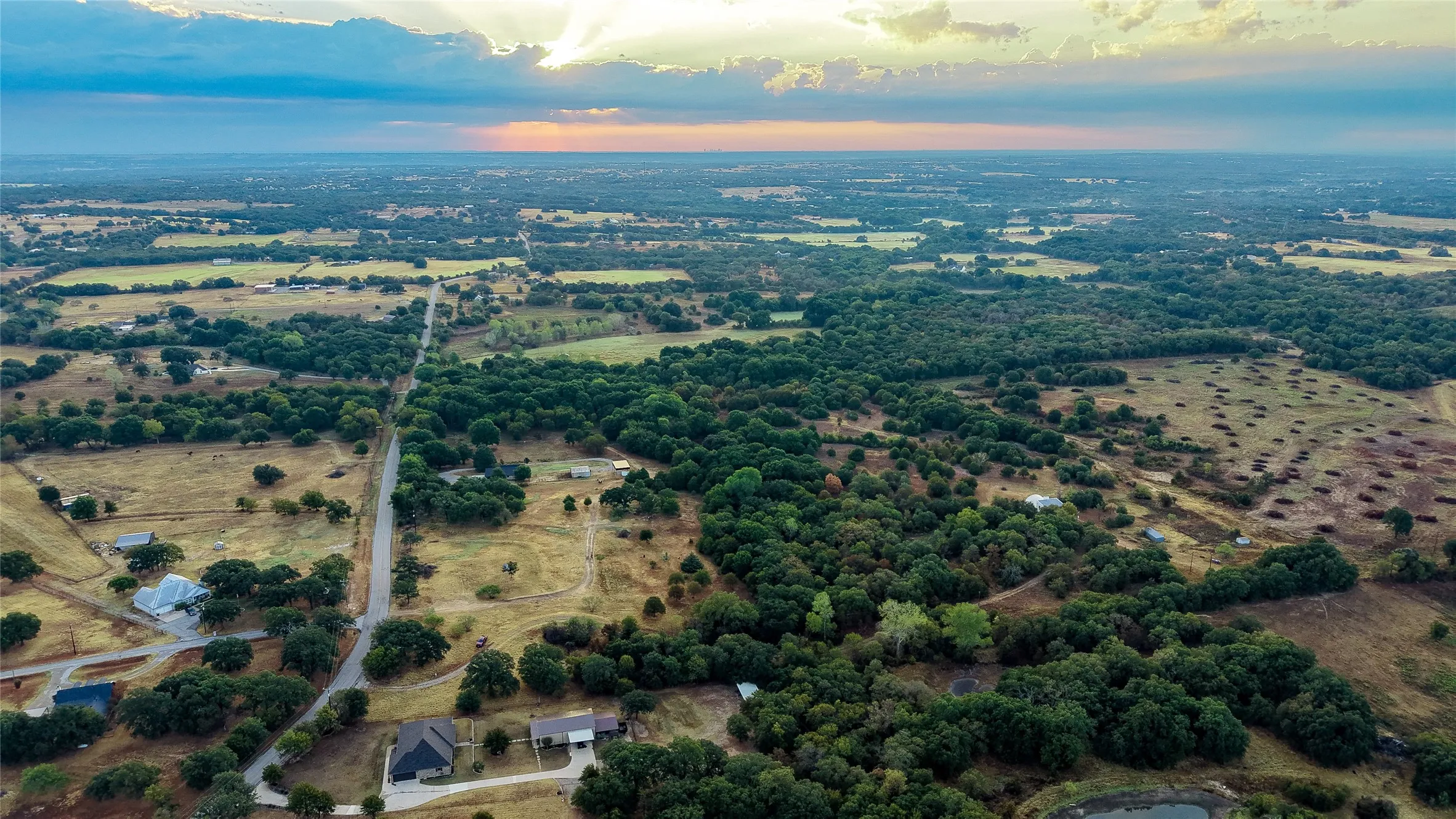 Expansive rural landscape featuring scattered residences, mature tree coverage, and open fields with a pond