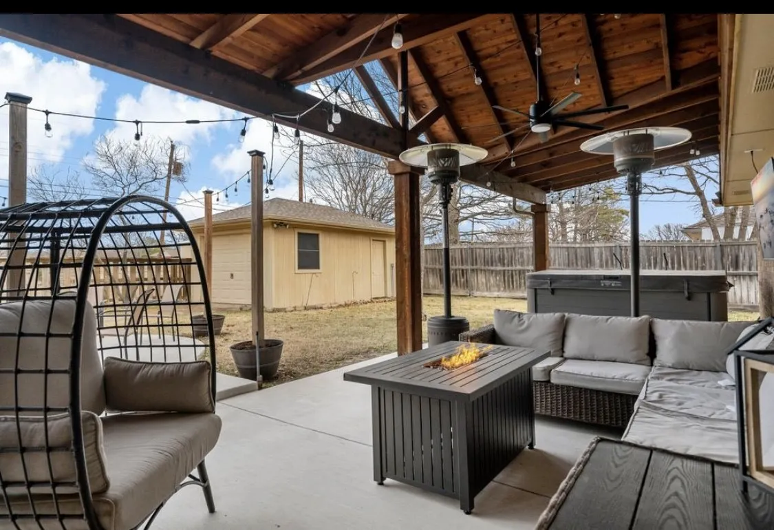 View of patio featuring ceiling fan, a fenced backyard, an outdoor structure, and an outdoor living space with a fire pit
