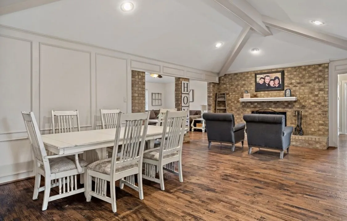 Dining area featuring vaulted ceiling with beams, a decorative wall, a brick fireplace, wood finished floors, and ornate columns