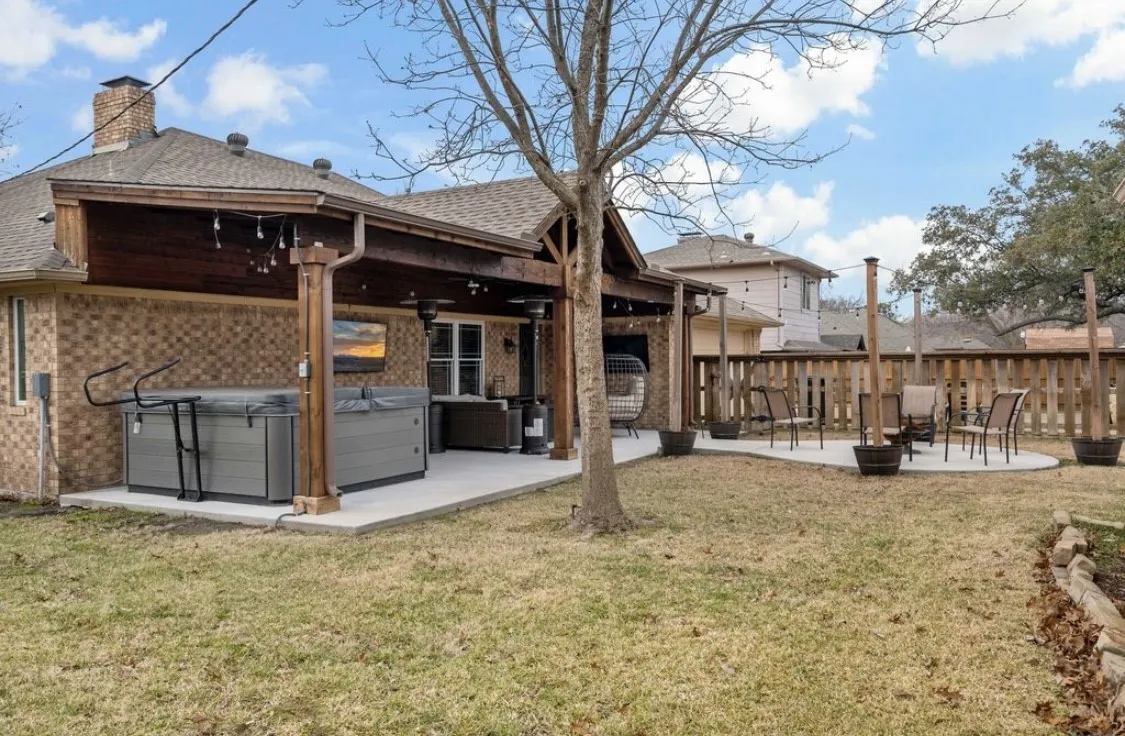 Back of house with brick siding, a patio, a lawn, a hot tub, and an outdoor fire pit