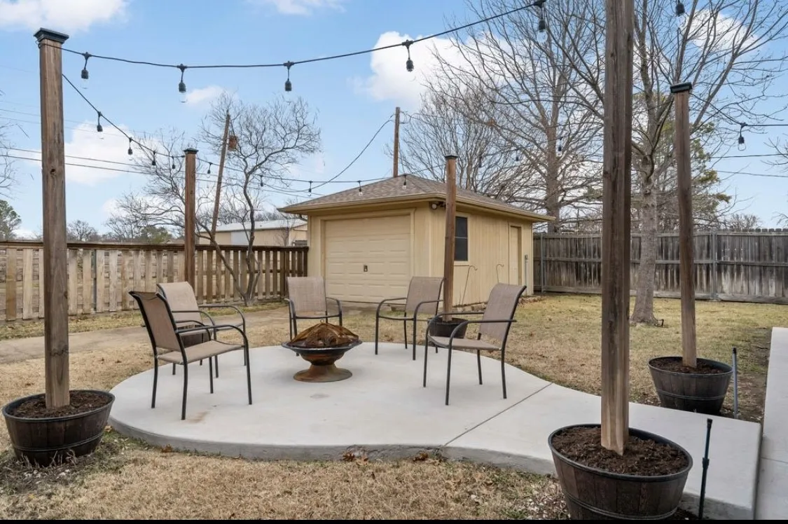 View of patio featuring a fenced backyard, an outdoor structure, a fire pit, and a detached garage