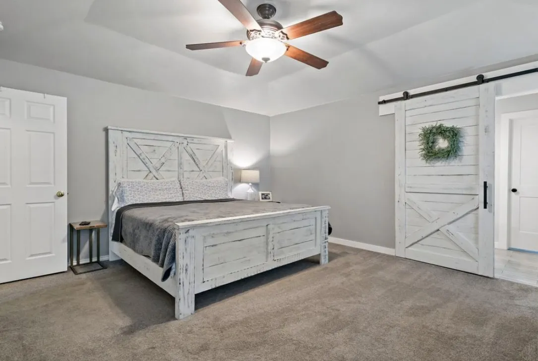 Carpeted bedroom with a barn door, baseboards, and a ceiling fan