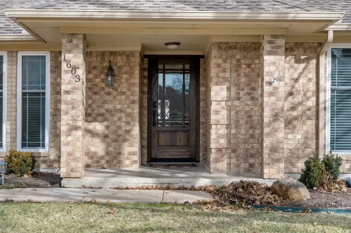 View of exterior entry with brick siding and roof with shingles