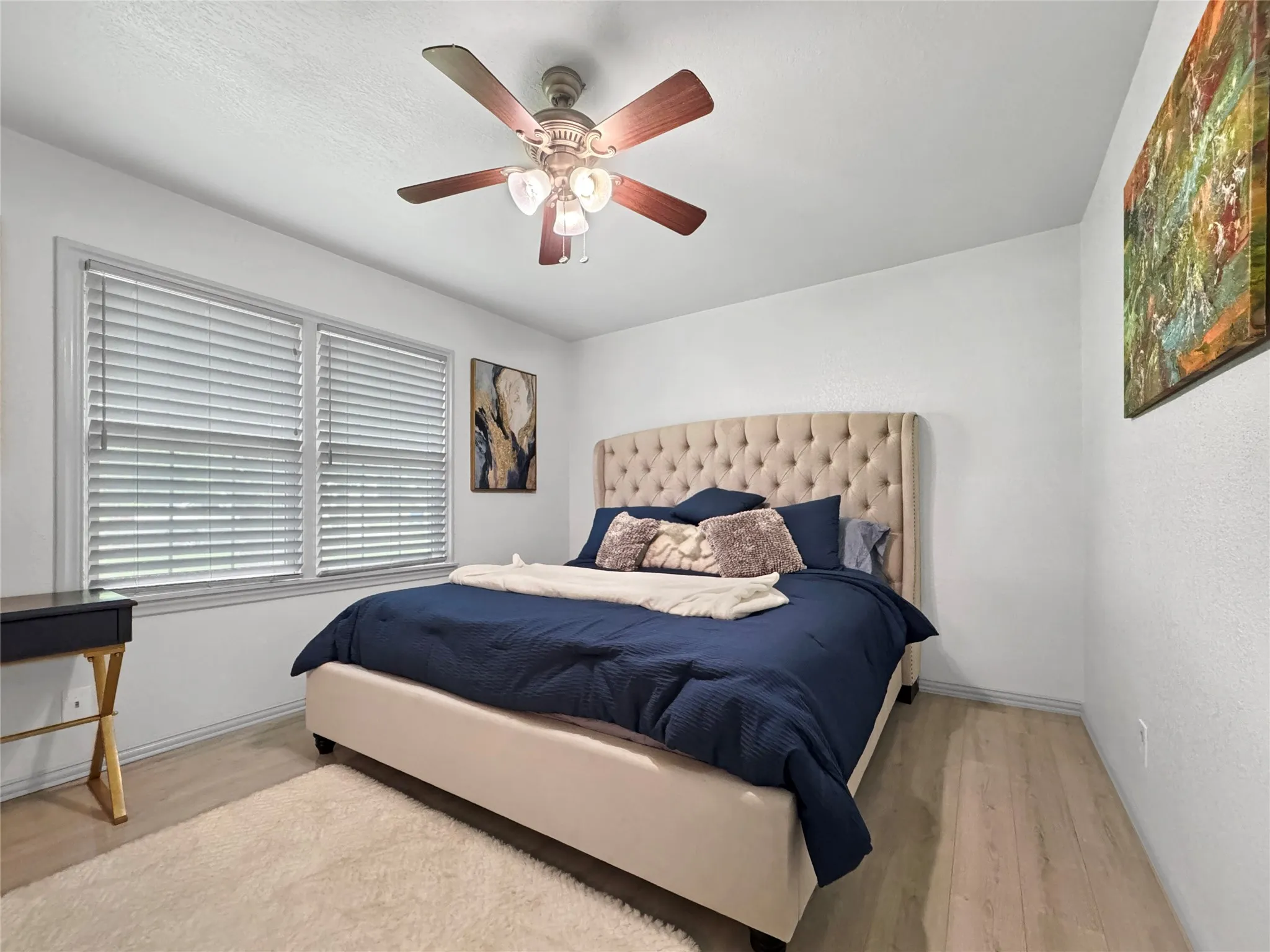 Wood-finish flooring, white walls, double windows with blinds, and a ceiling fan with integrated lighting