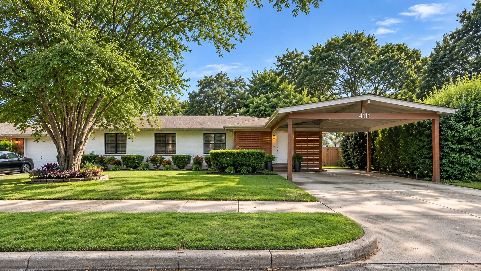 Well-maintained front lawn with mature trees, a covered carport, and a brick exterior accent