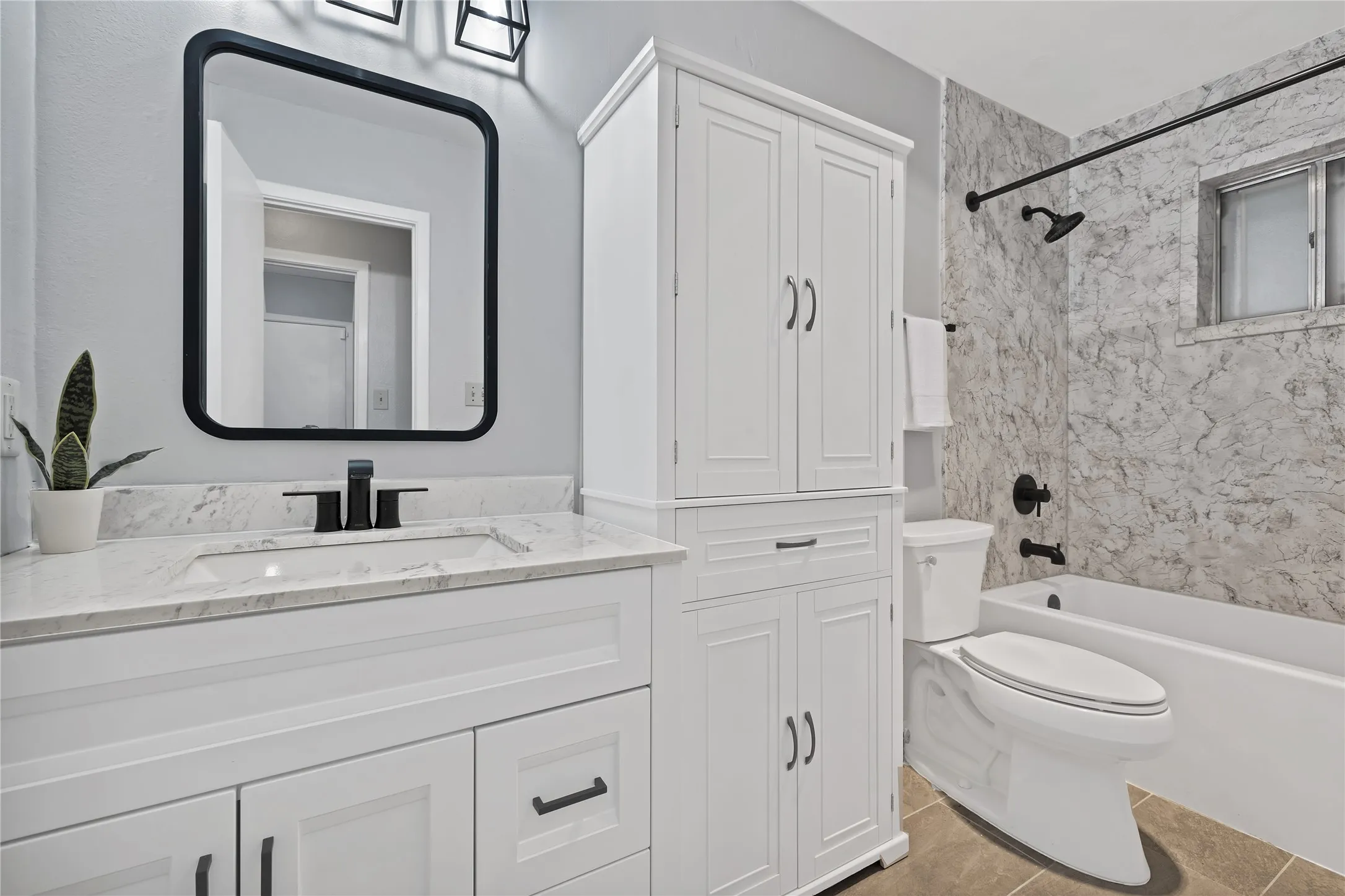 Bathroom: Updated bath with white shaker vanity, marble-look countertop, and matte black faucet and fixtures. Tall linen cabinet, tile flooring, and marble-look tub surround.