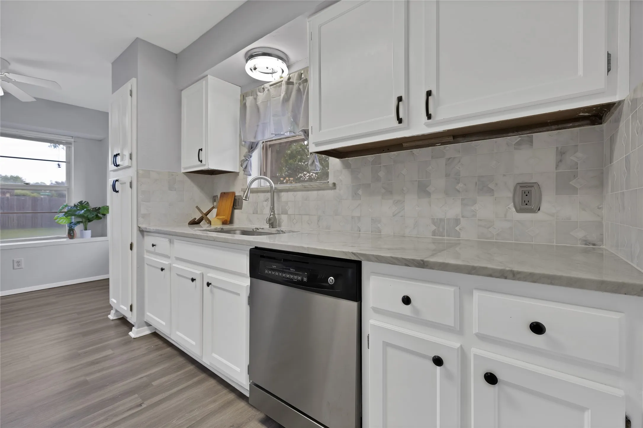 Kitchen: White painted cabinetry with black hardware, veined stone countertops, and marble tile backsplash. Undermount stainless steel sink with pull-down faucet and window above.