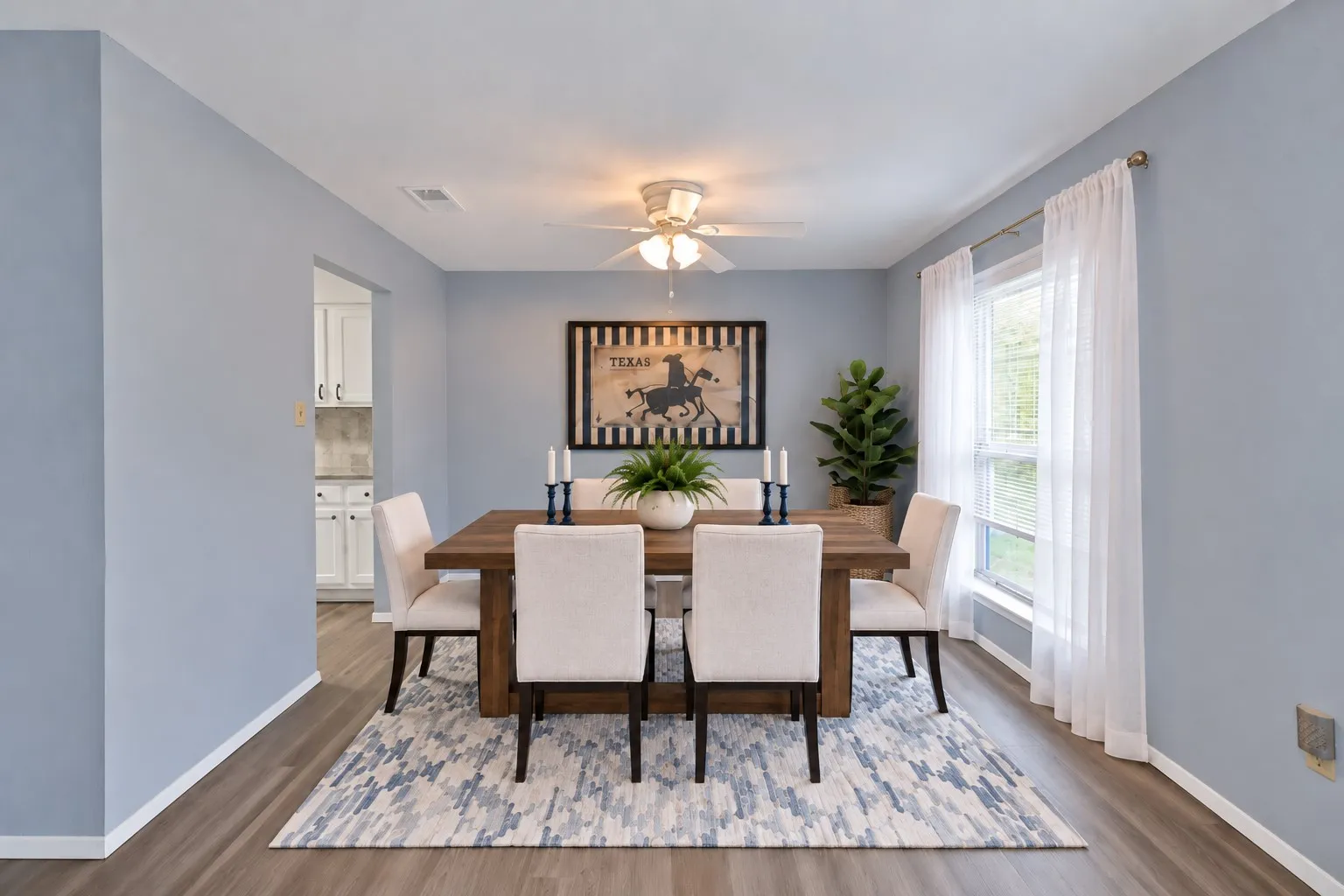 Dining room: Dining room with ceiling fan, front-facing window, and wood-look plank flooring. Cased opening to the kitchen. Virtually staged.