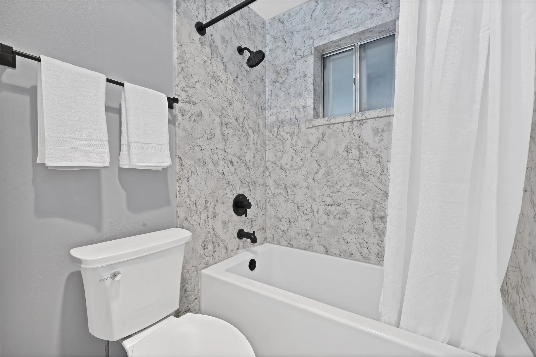 Bathroom: Tub and shower combo with marble-look wall panels, matte black showerhead and trim, and window.