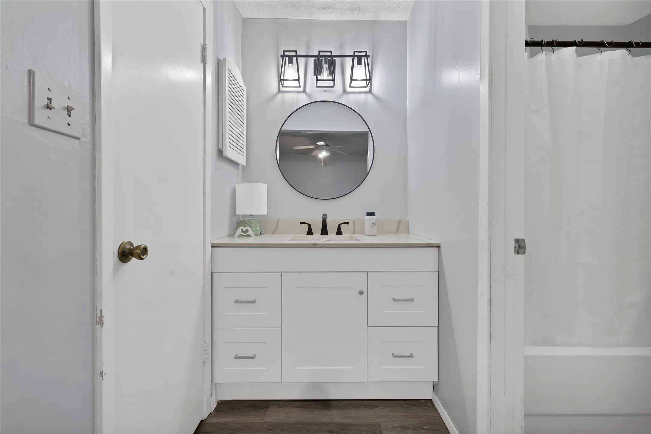 Bathroom vanity: White shaker vanity with matte black faucet, round black mirror, and black cage vanity light. Separate tub and shower area.