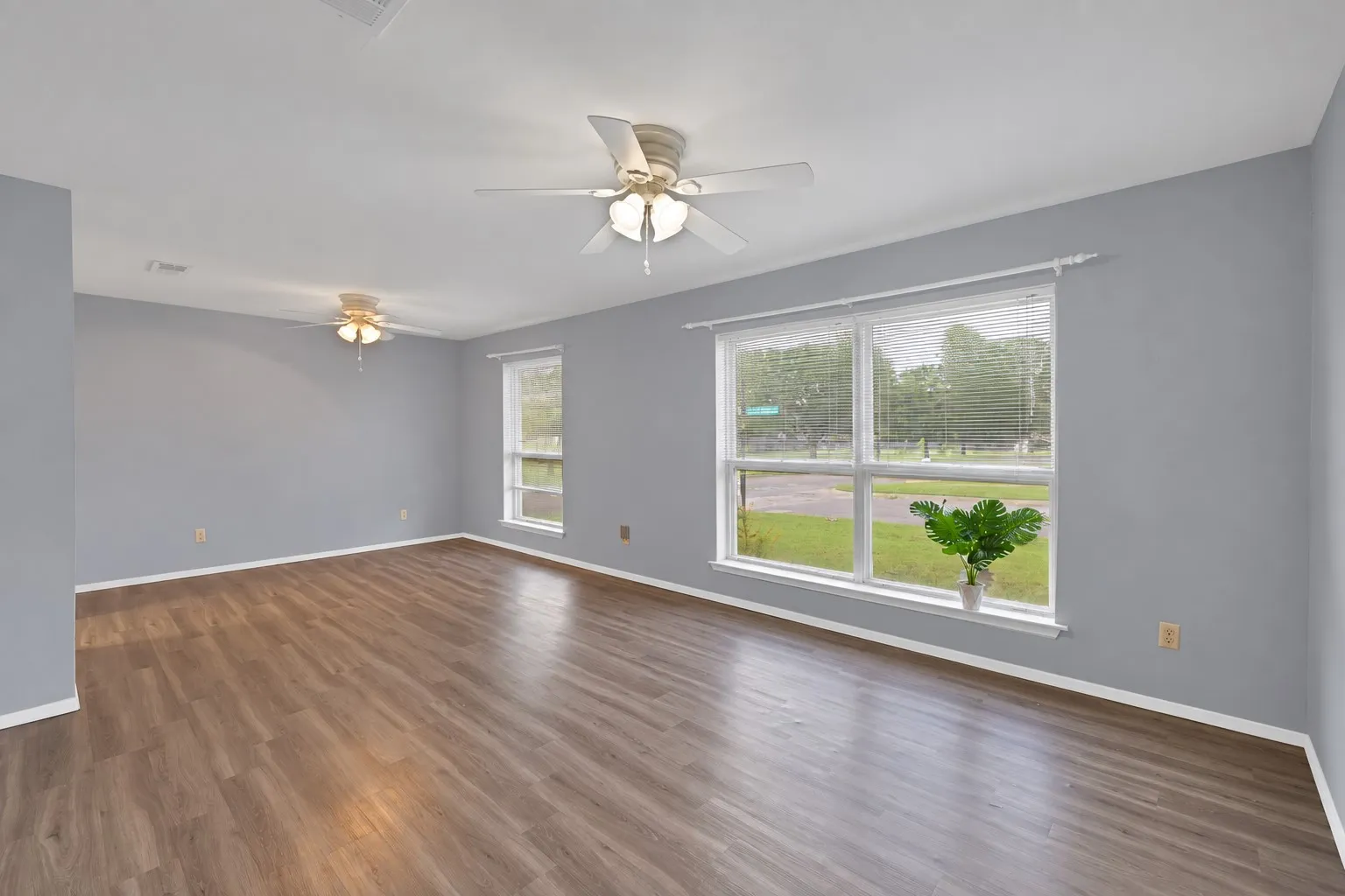 Living and dining: Front living and dining area with wood-look plank flooring, two ceiling fans, and a large front window. Doorway connects directly to the kitchen.