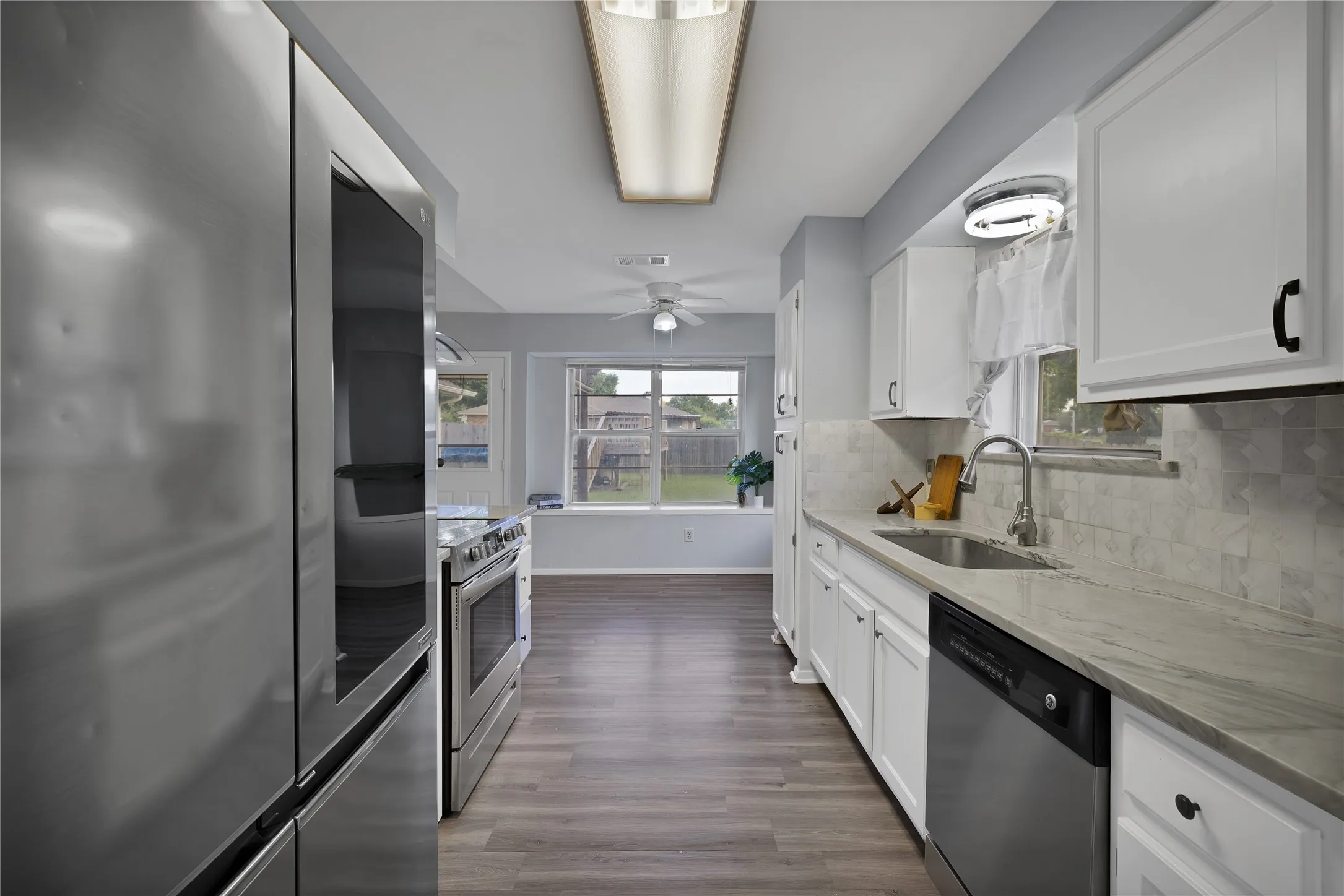 Kitchen: Galley kitchen with white painted cabinetry, veined stone countertops, and marble tile backsplash. LG stainless steel refrigerator, stainless steel range, and GE dishwasher, opening to the breakfast area.