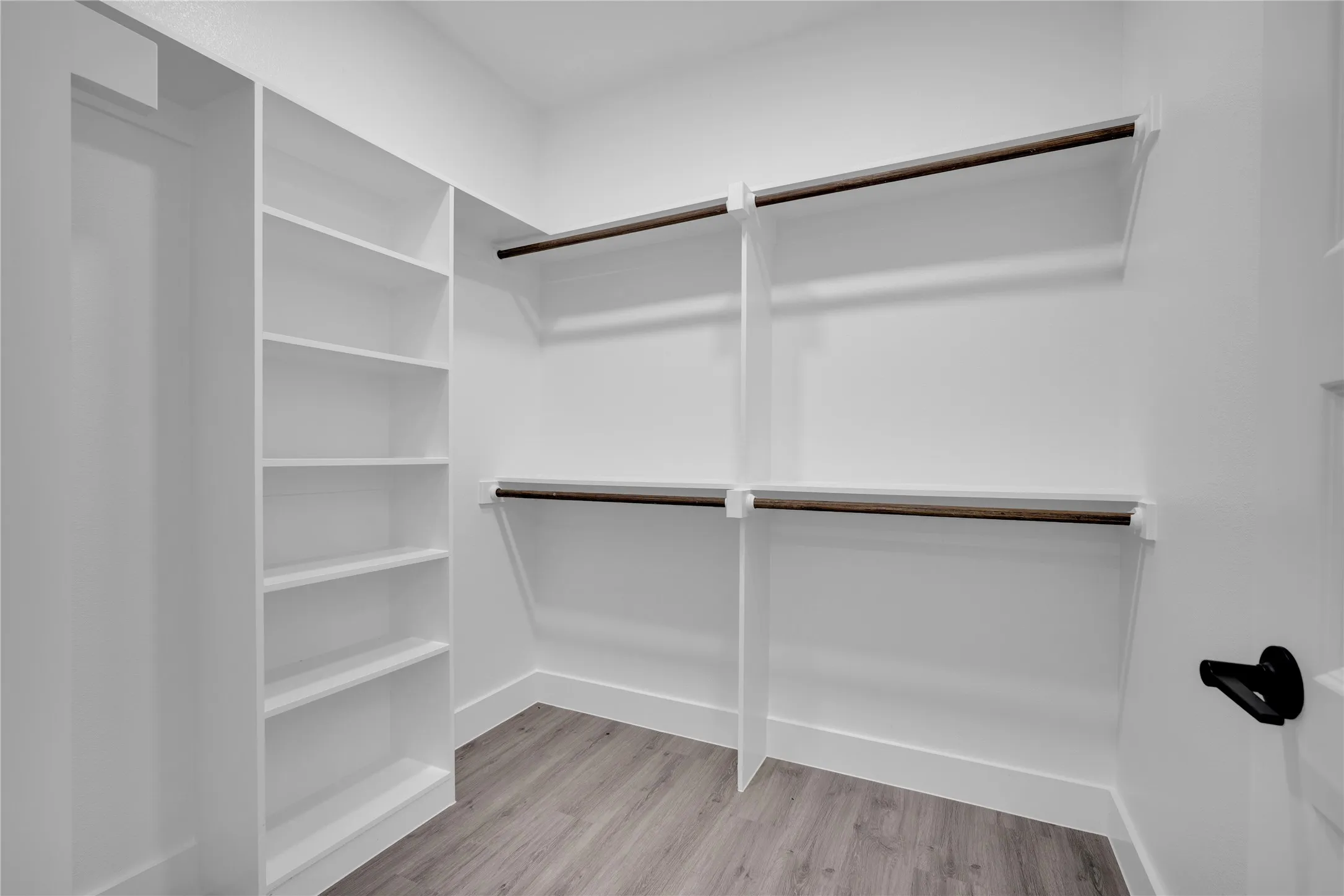 Built-in shelving, multiple hanging rods, and wood-finish flooring