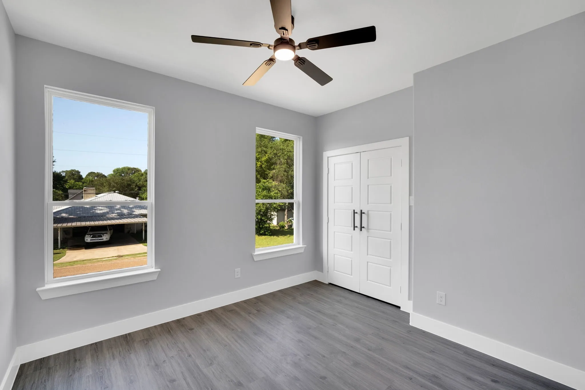 Wood-finish flooring, two large windows, white trim, a ceiling fan with light, and paneled double doors