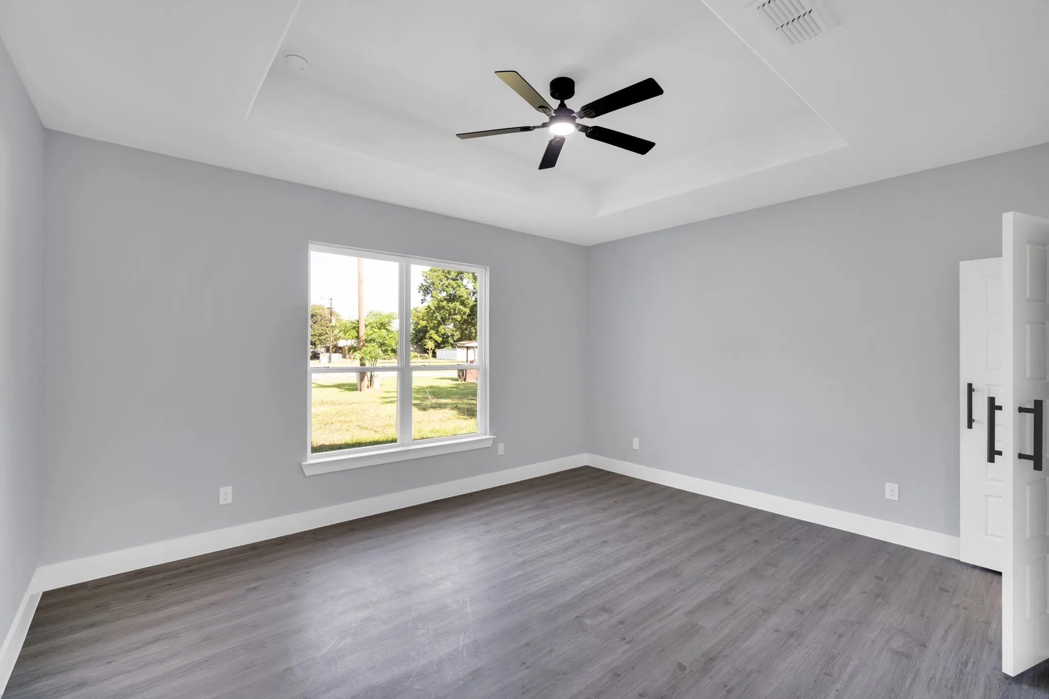 Tray ceiling with a ceiling fan, wood-finish flooring, white trim, and a window providing natural illumination