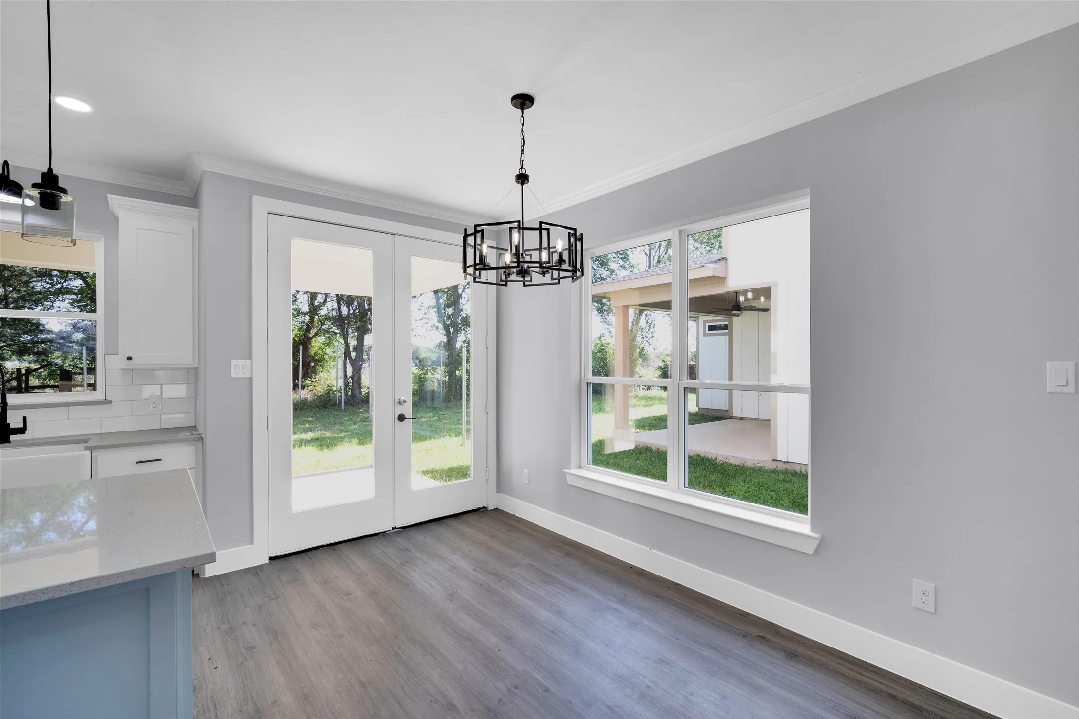 Wood-finish flooring, contemporary chandelier, double glass-paneled doors, large framed window, and crown molding