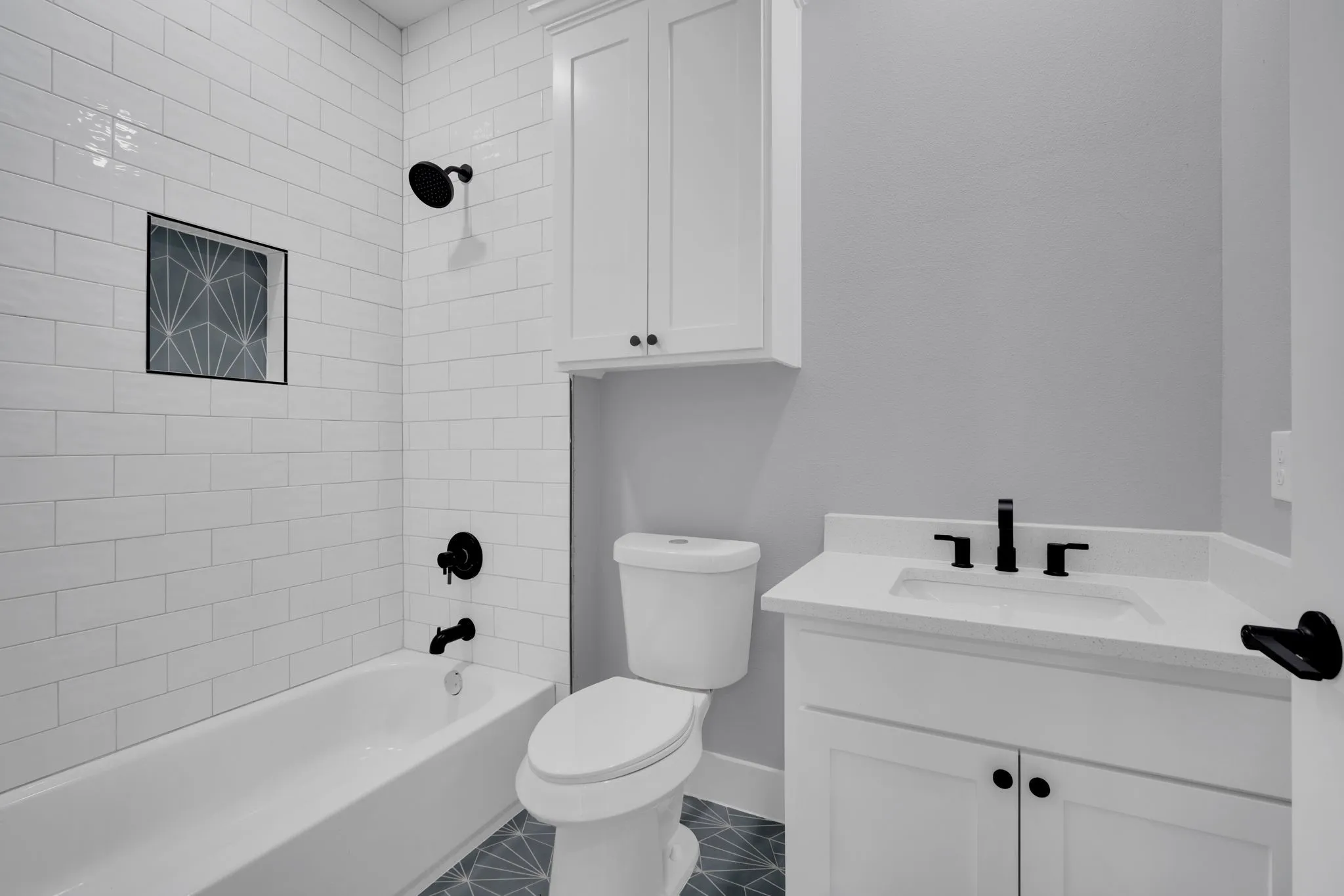 White subway tile shower surround with black fixtures, white vanity with integrated sink, patterned floor tile, and built-in storage cabinetry