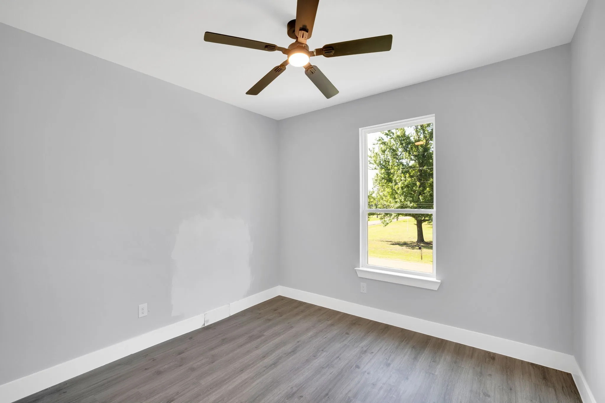 Wood-finish flooring with white trim, a single window, and a ceiling fan with integrated lighting