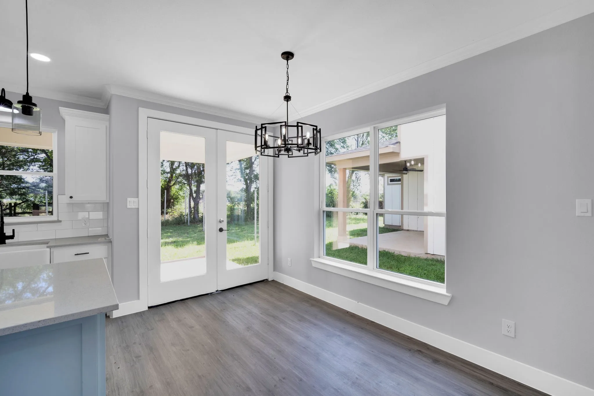 Wood-finish flooring, white French doors, large windows, recessed ceiling lighting, and a contemporary chandelier