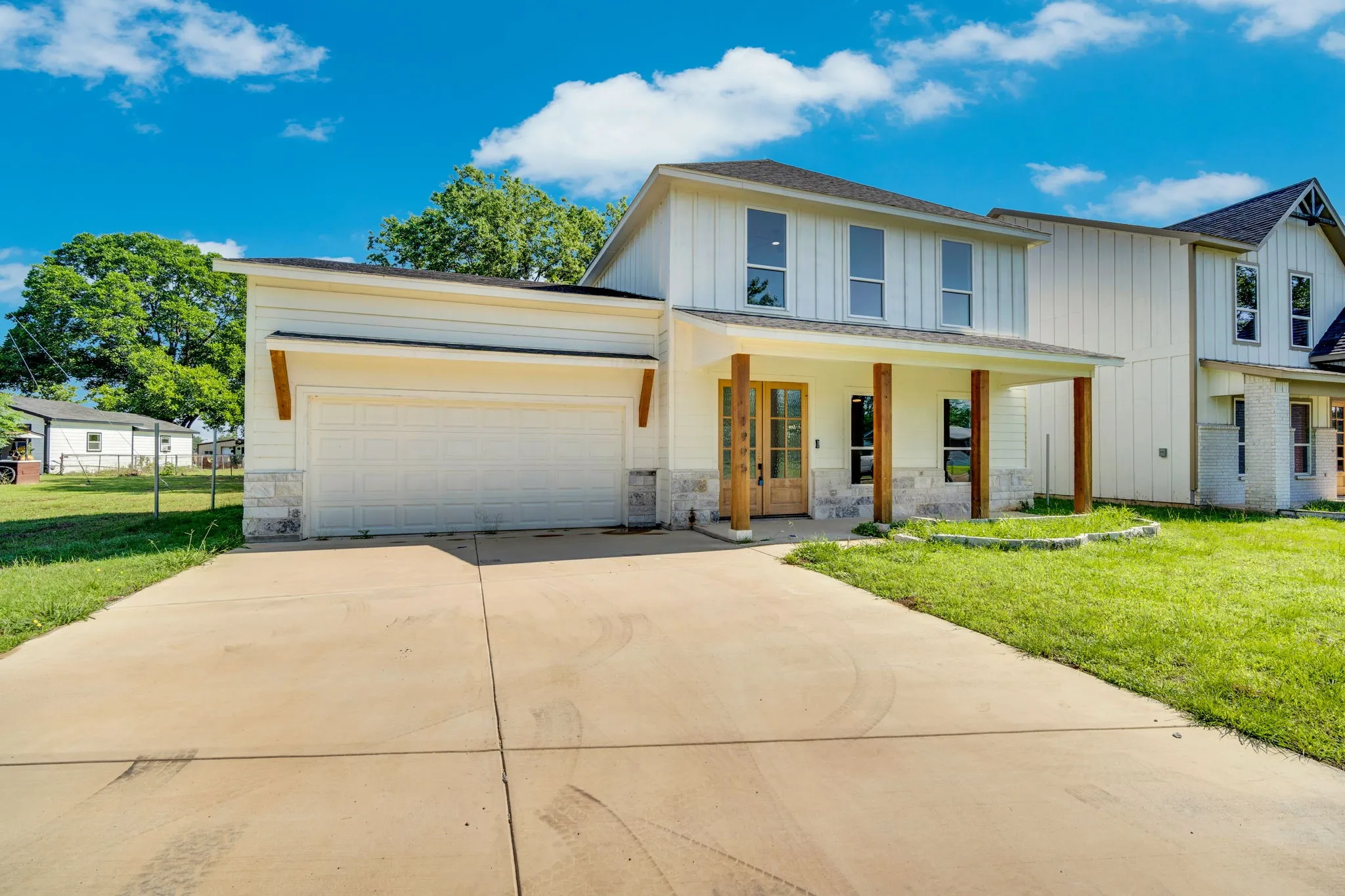 Two-story exterior with board and batten siding, stone facade accents, covered front porch with wood columns, and a two-car garage