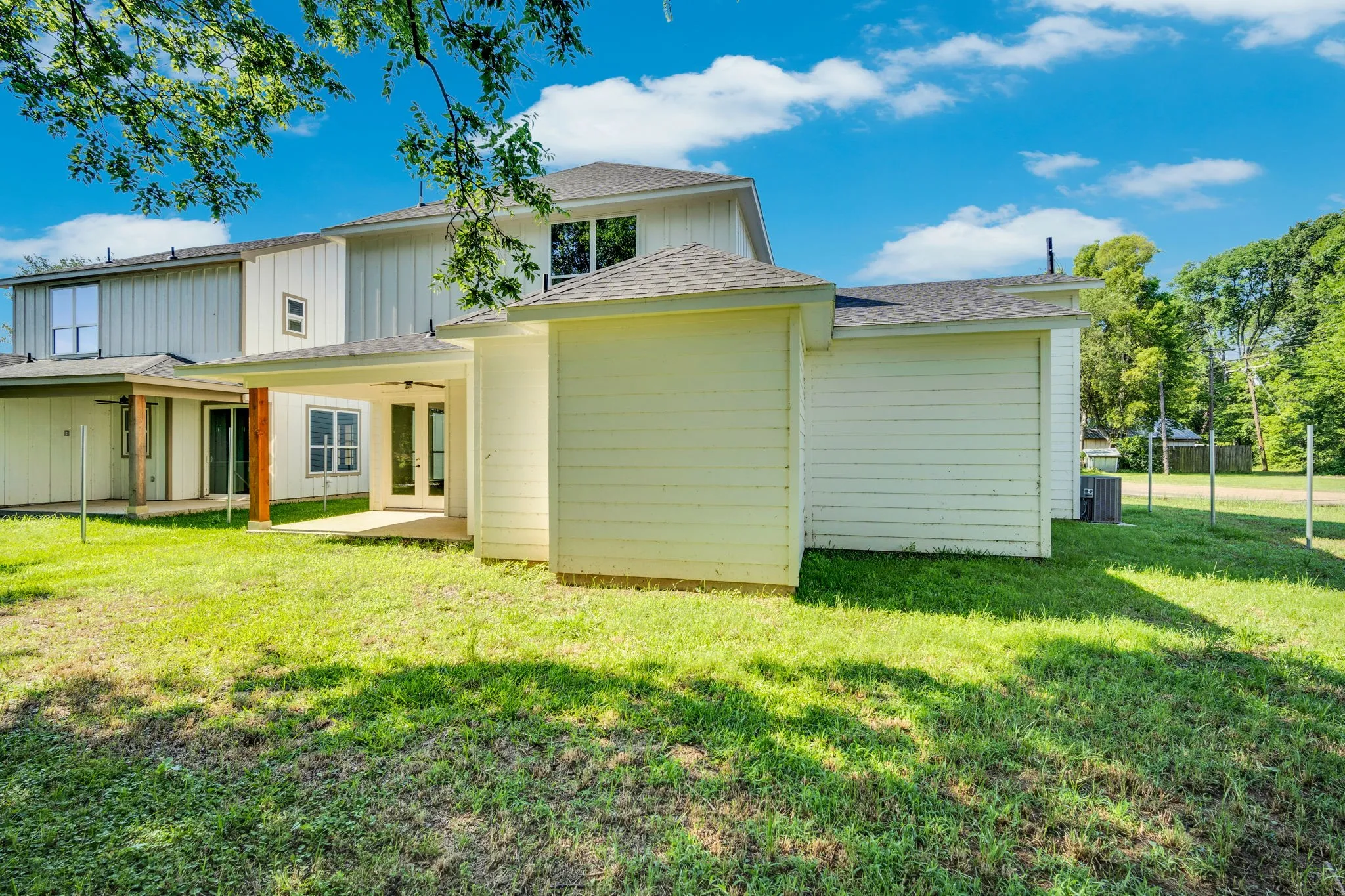Expansive grassy area with a covered patio, featuring a ceiling fan and a wood support column