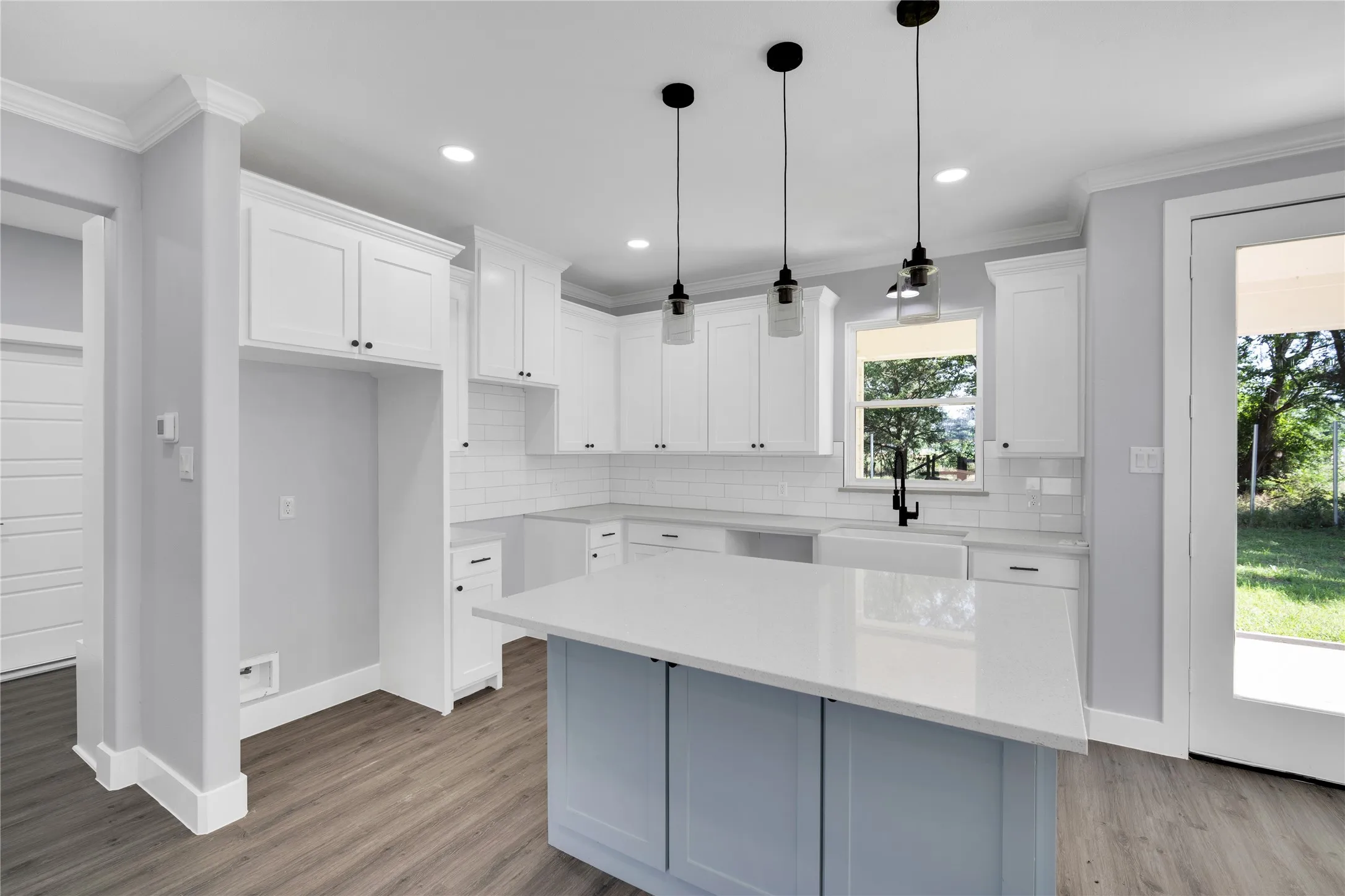 Kitchen featuring a center island with a light-toned countertop, white cabinetry with dark hardware, subway tile backsplash, and wood-finish flooring