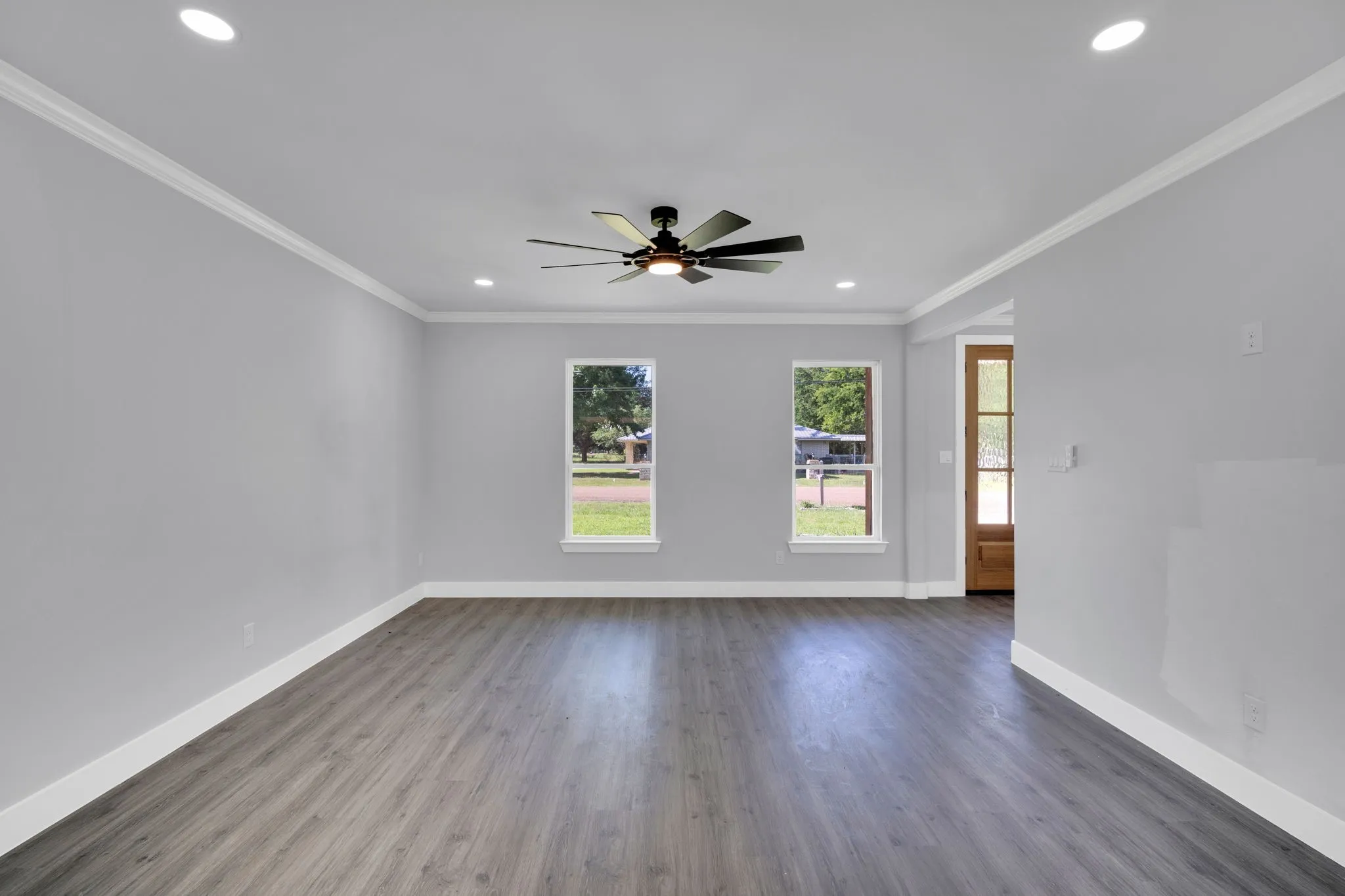 Recessed ceiling lighting, wood-finish flooring, two windows, ceiling fan with integrated lighting, and a wood entry door with frosted glass panels