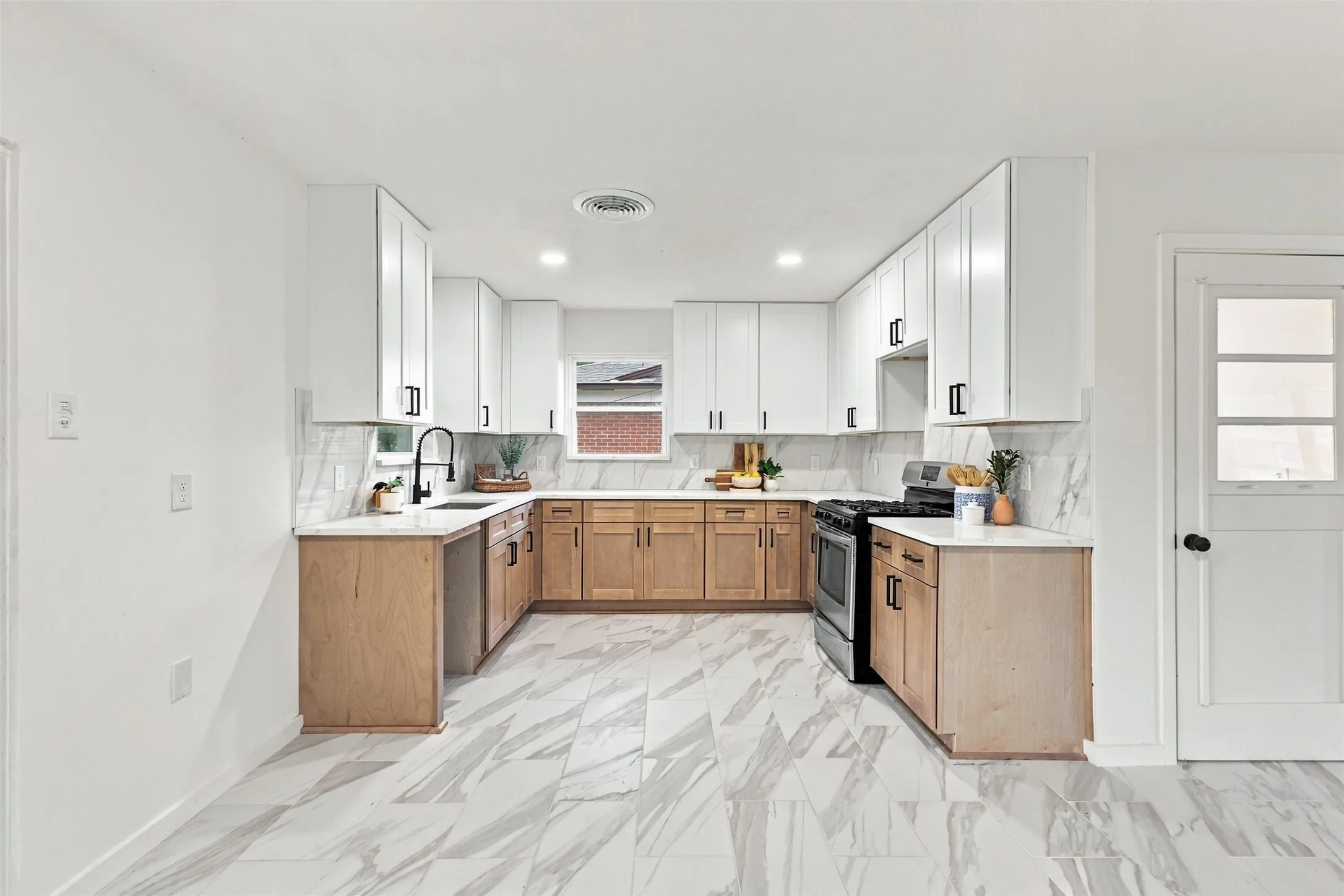 U-shaped kitchen with white upper cabinetry, natural wood-finish lower cabinetry, light-toned countertops, tile backsplash, and patterned tile flooring