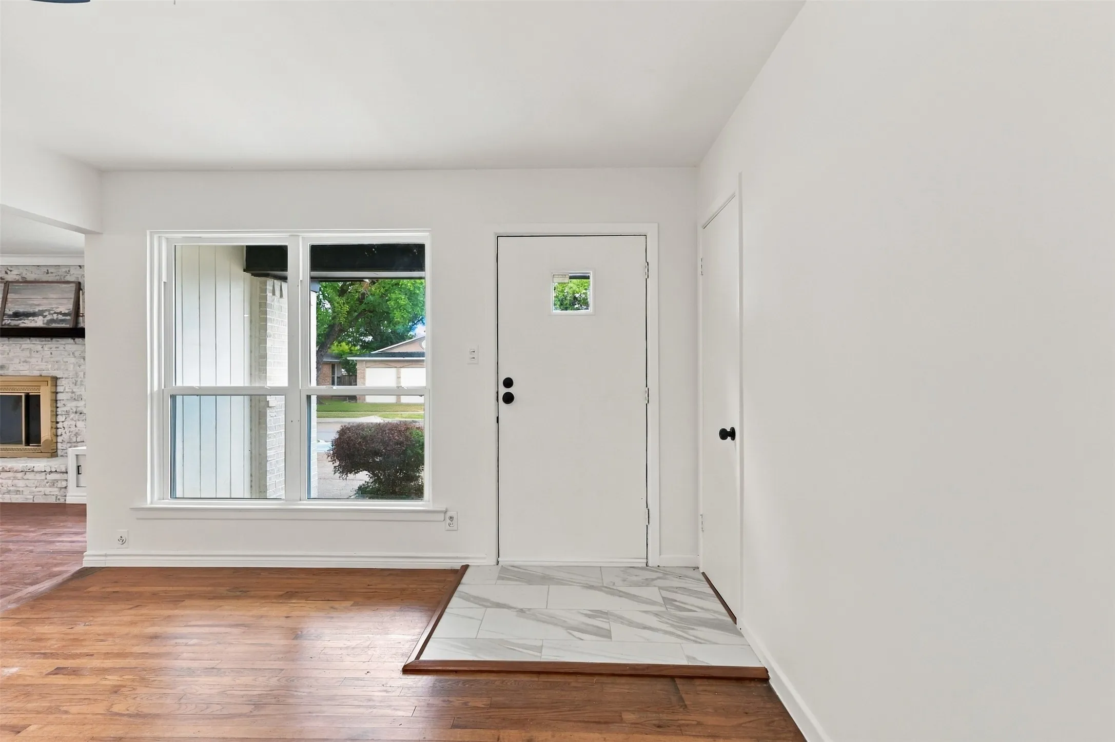 Entryway featuring wood-finish flooring, a white door with a small window, and a white tiled landing