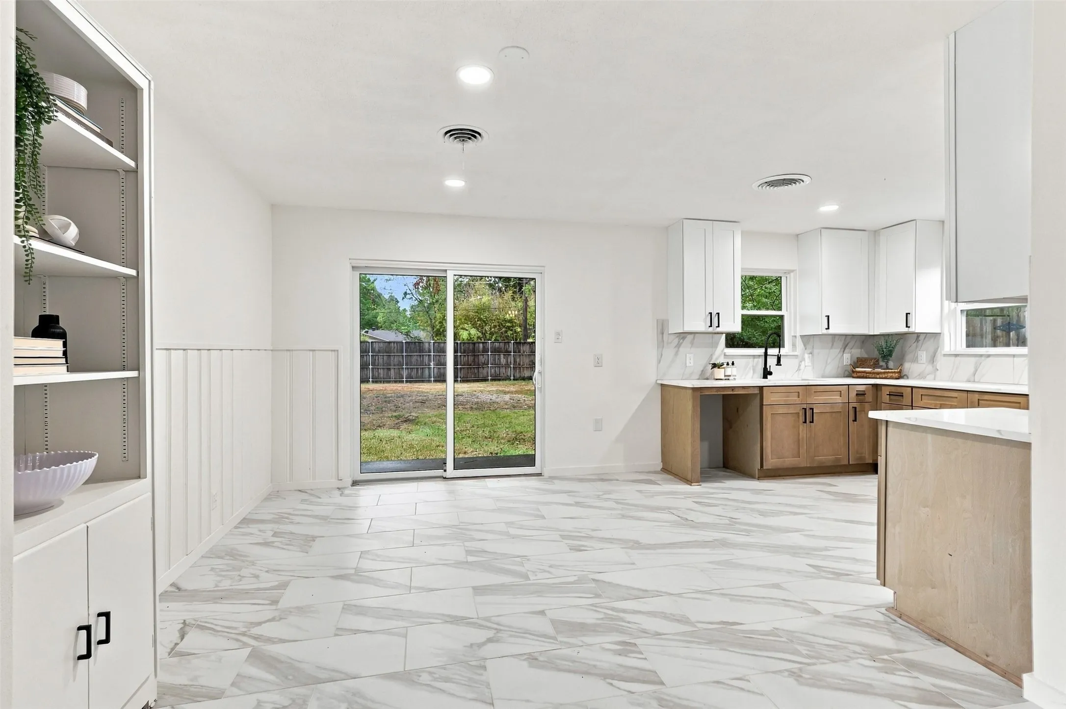 White cabinetry, wood-finish lower cabinets, white tile flooring, sliding glass door, and a built-in shelving unit