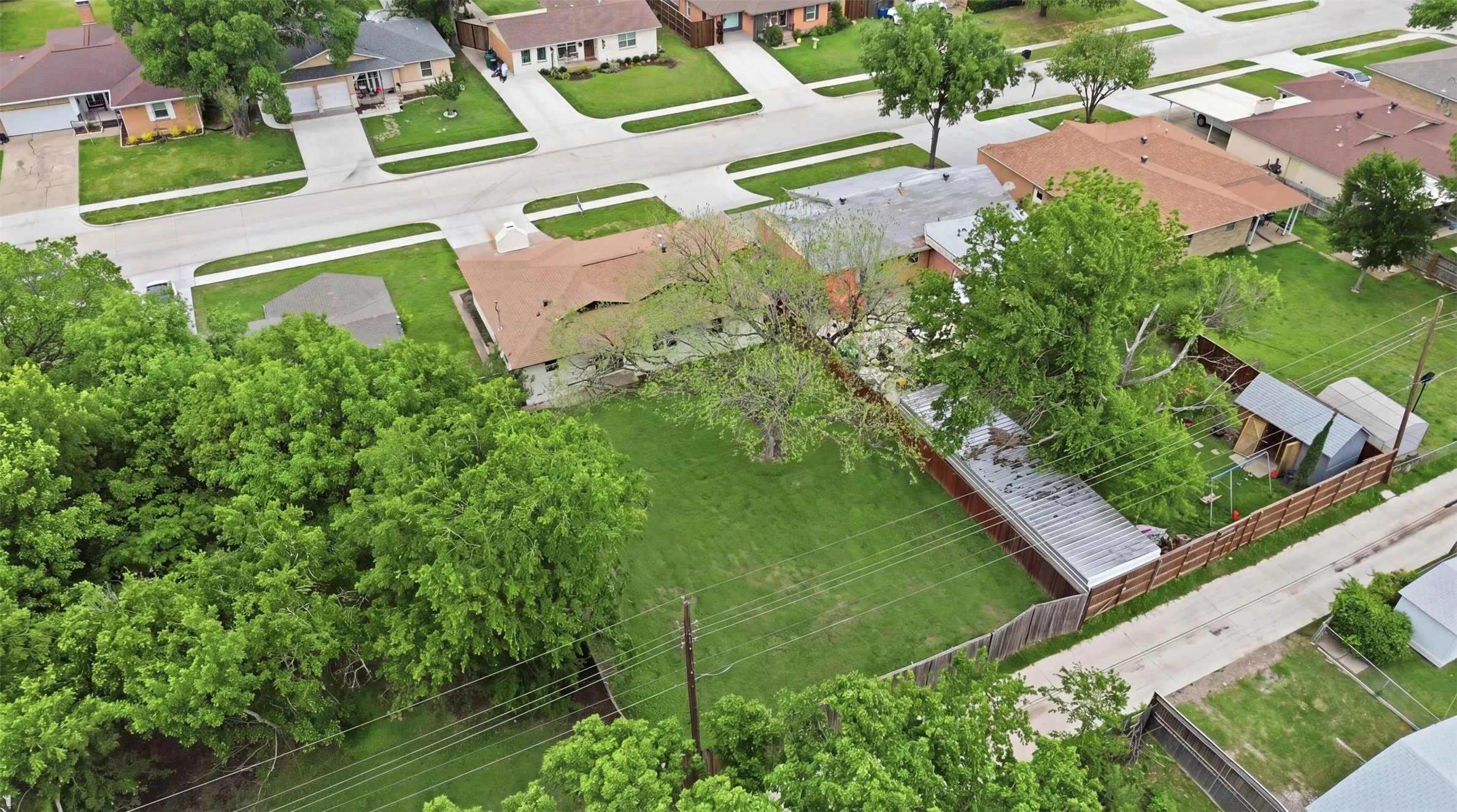 Expansive grassy lot featuring mature trees and a perimeter fence