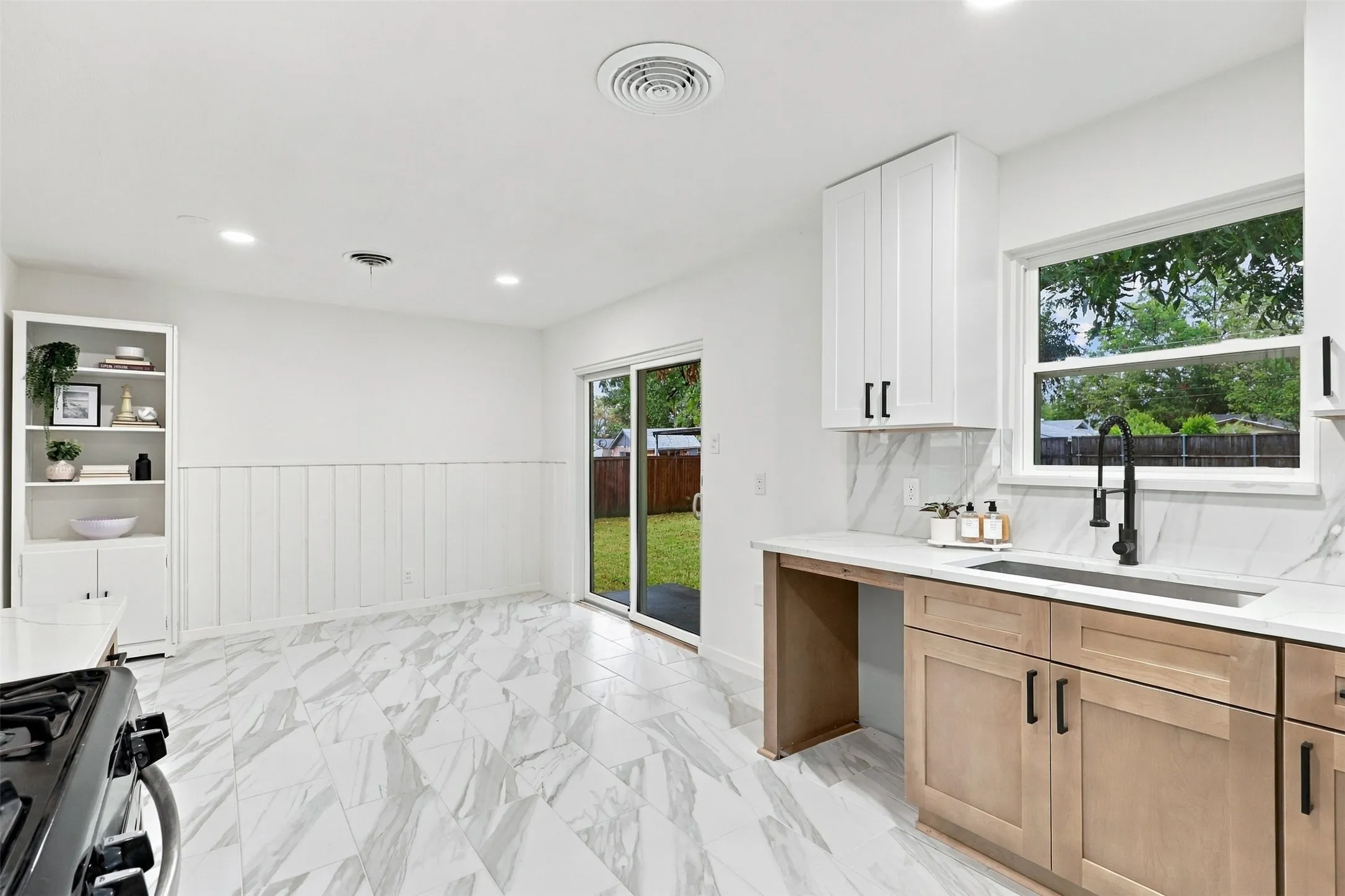 Bright, open kitchen showcasing marble-look flooring, white shaker cabinetry with black hardware, quartz countertops, and a black matte faucet