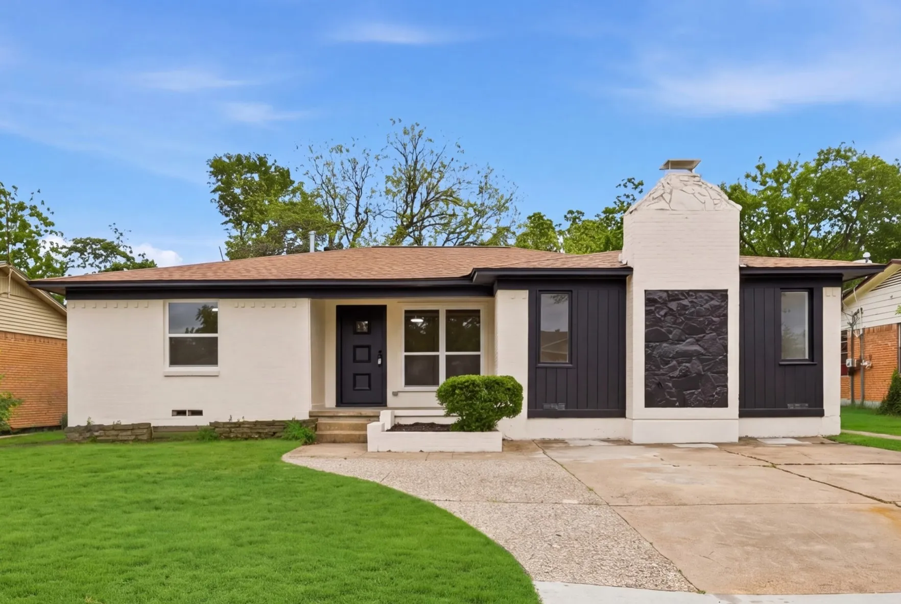 Single-story exterior with white brick, dark trim, a prominent chimney with sculptural detailing, and a paved driveway
