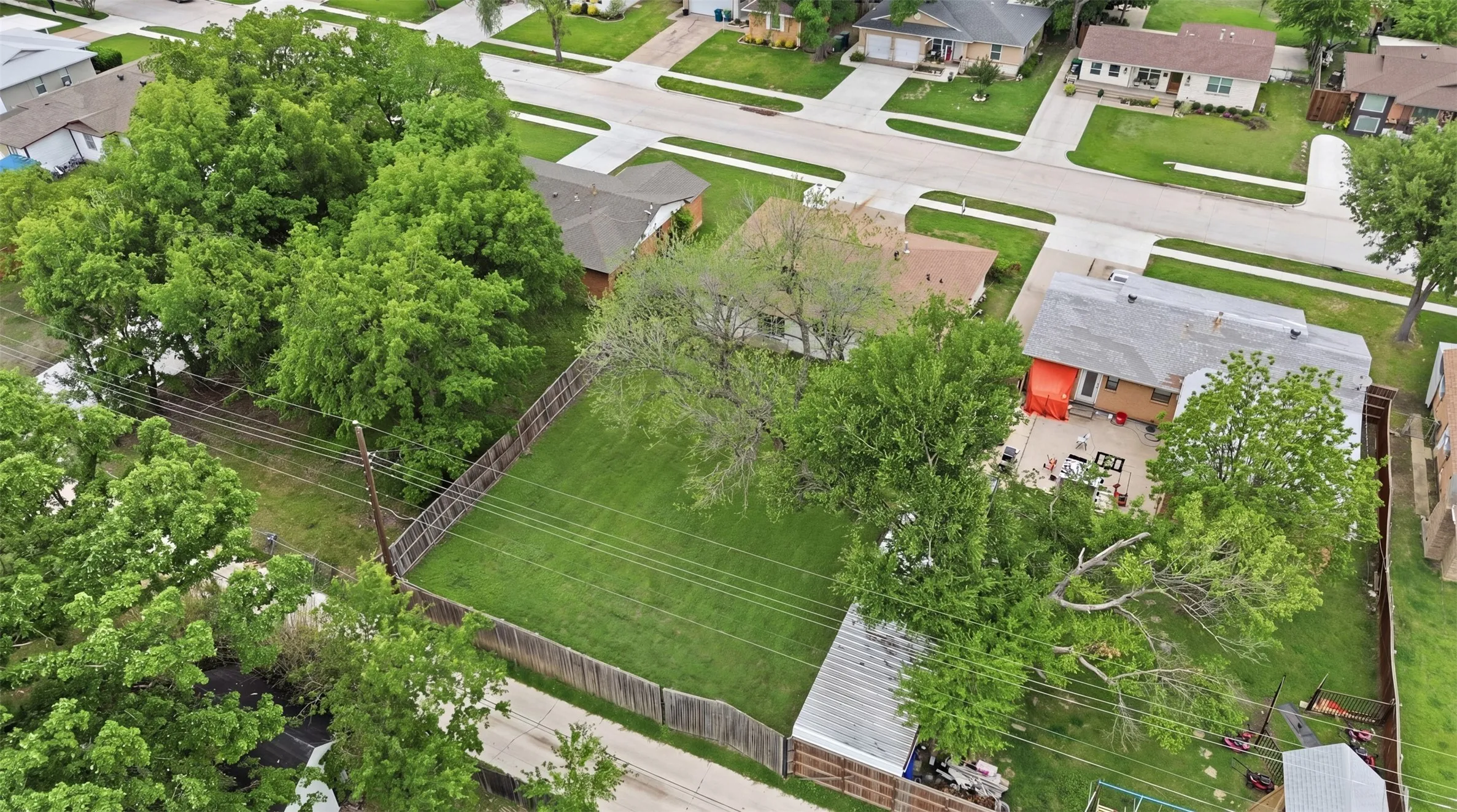 Expansive grassy lot bordered by a wood fence, featuring mature trees